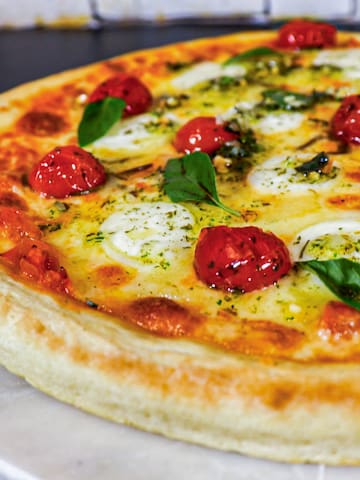 a pizza with tomatoes and basil on a marble plate