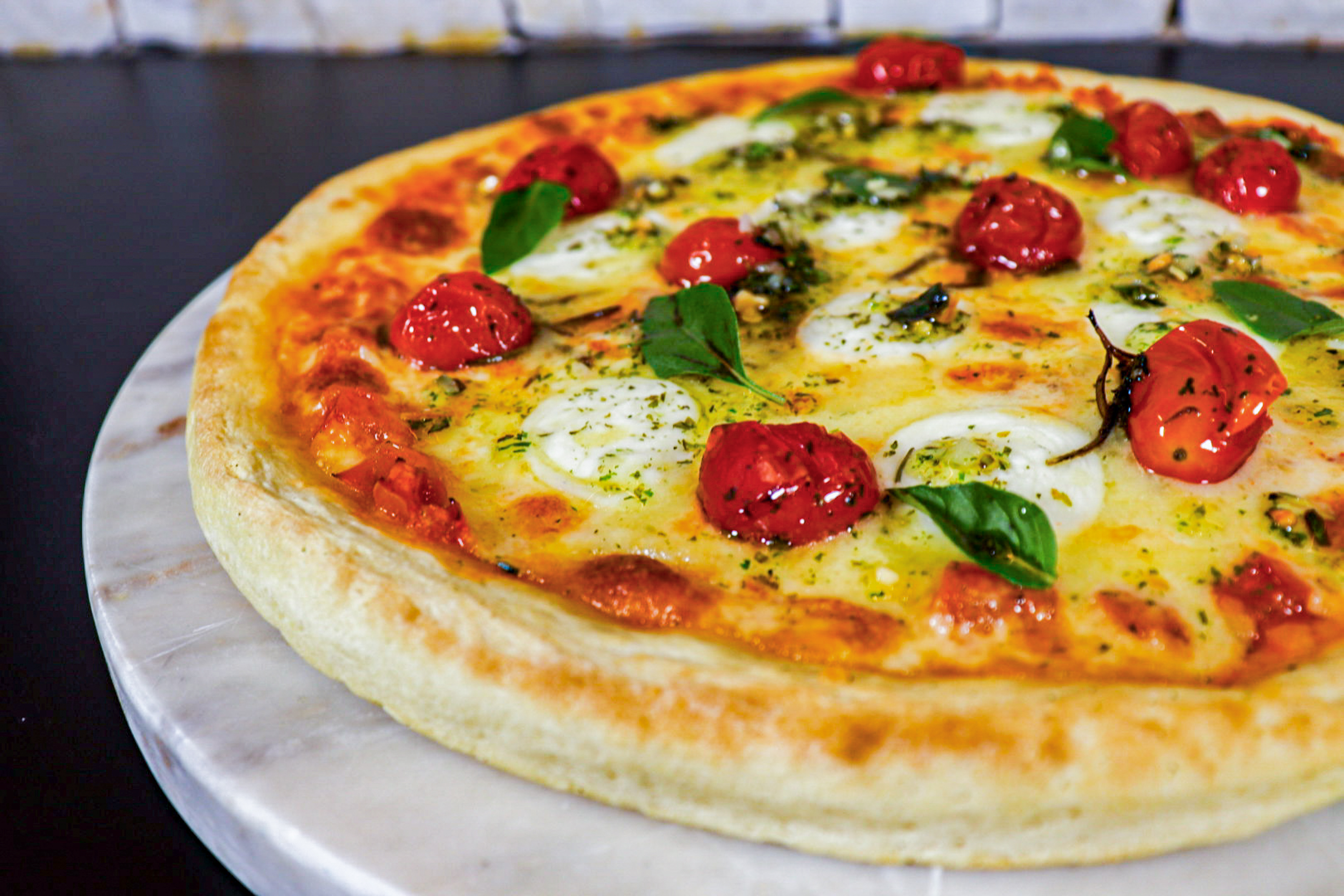 a pizza with tomatoes and basil on a marble plate