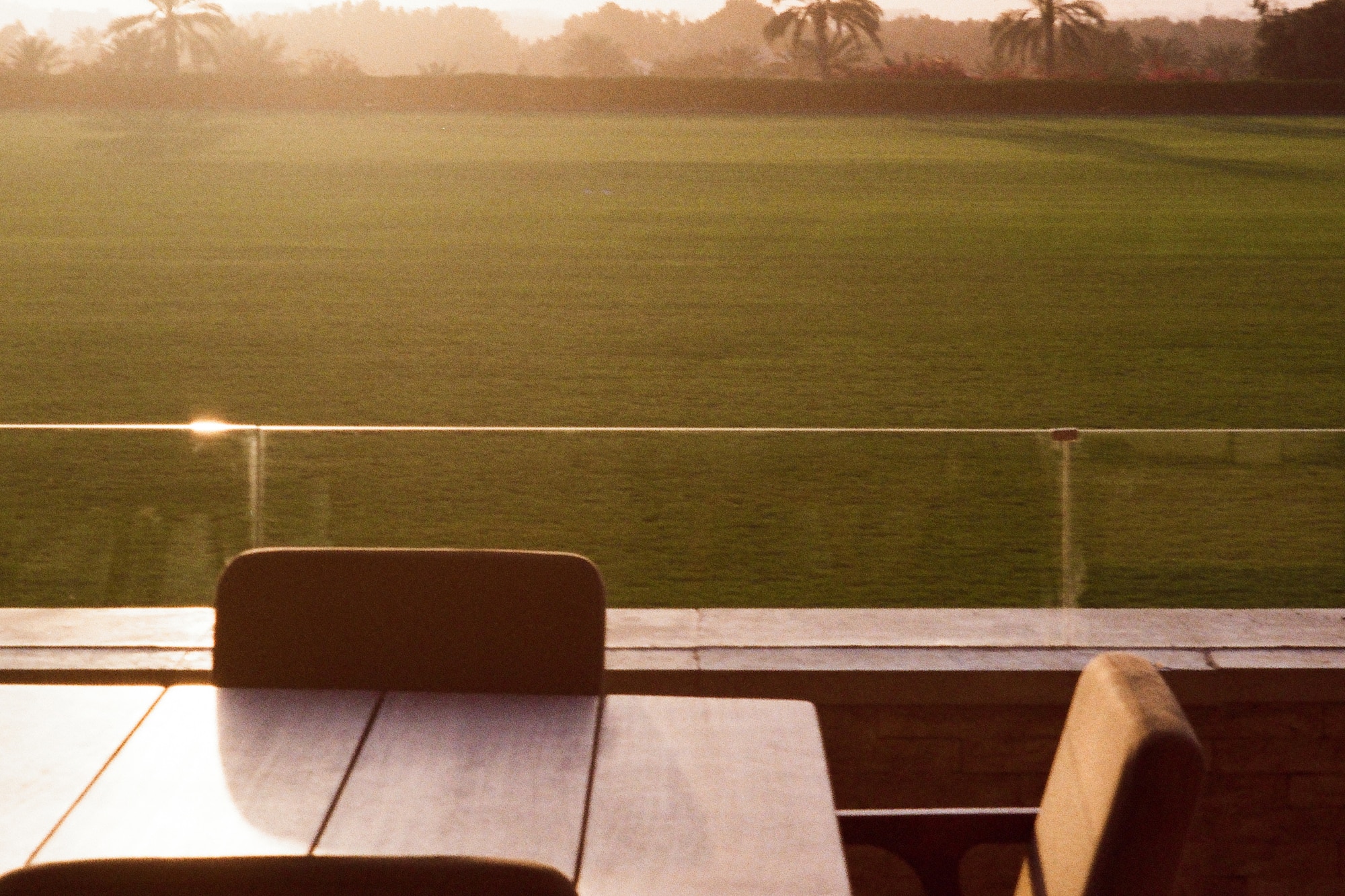 Outdoor patio dining overlooking a green golf course and palm trees at sunset.