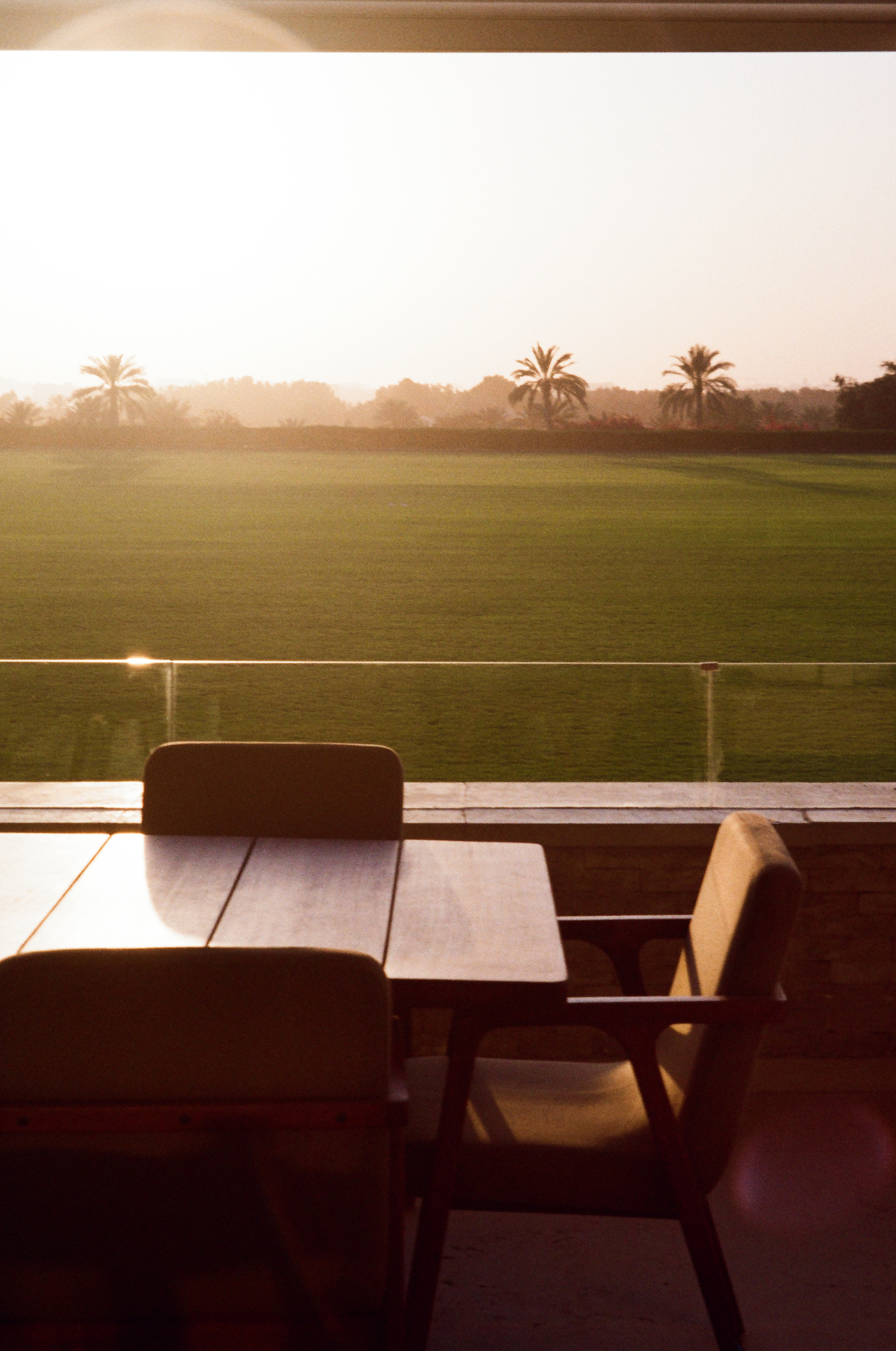 Outdoor patio dining overlooking a green golf course and palm trees at sunset.