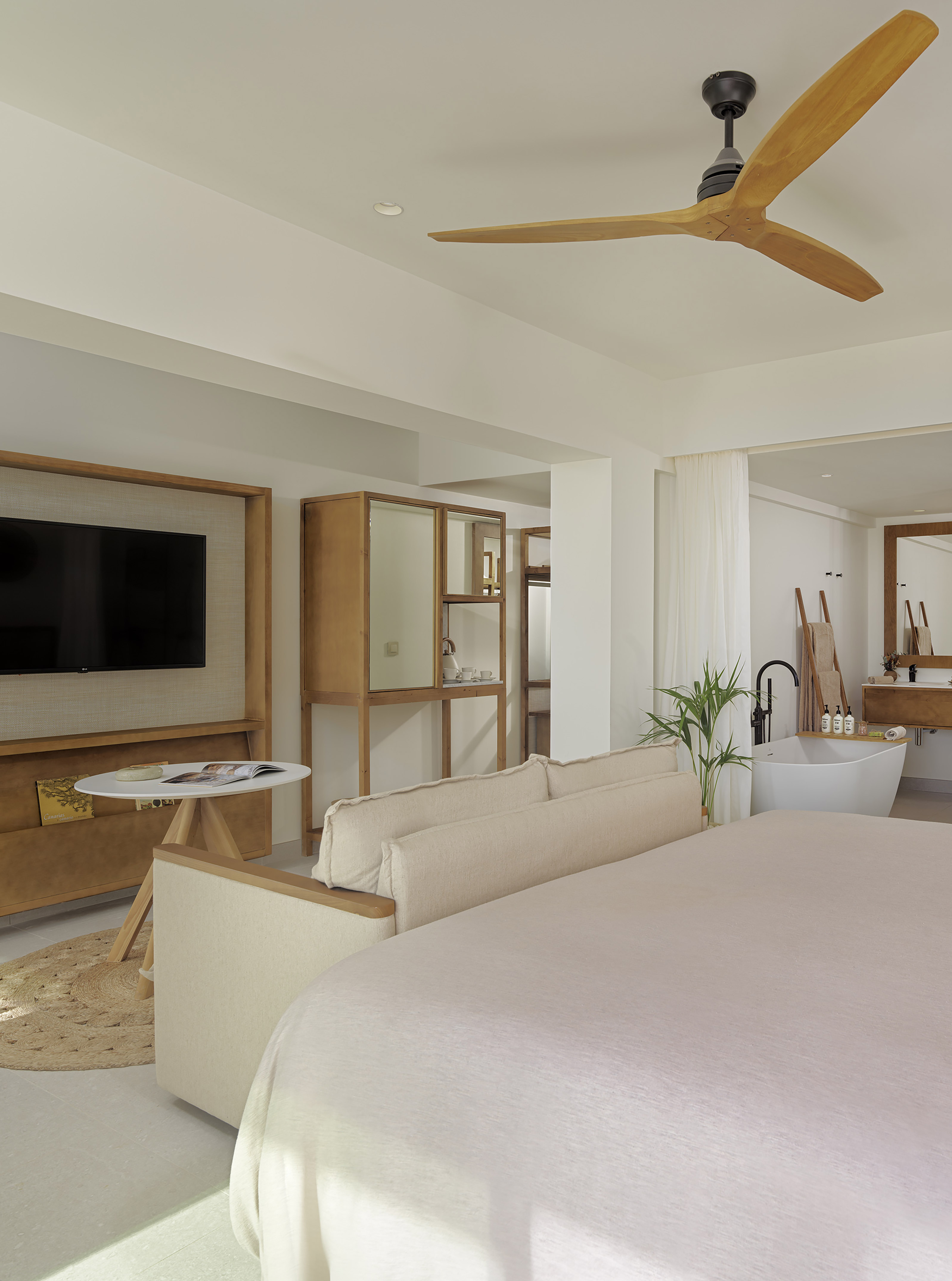 Bright bedroom suite with bed, TV, wood fan, and open-concept tub.
