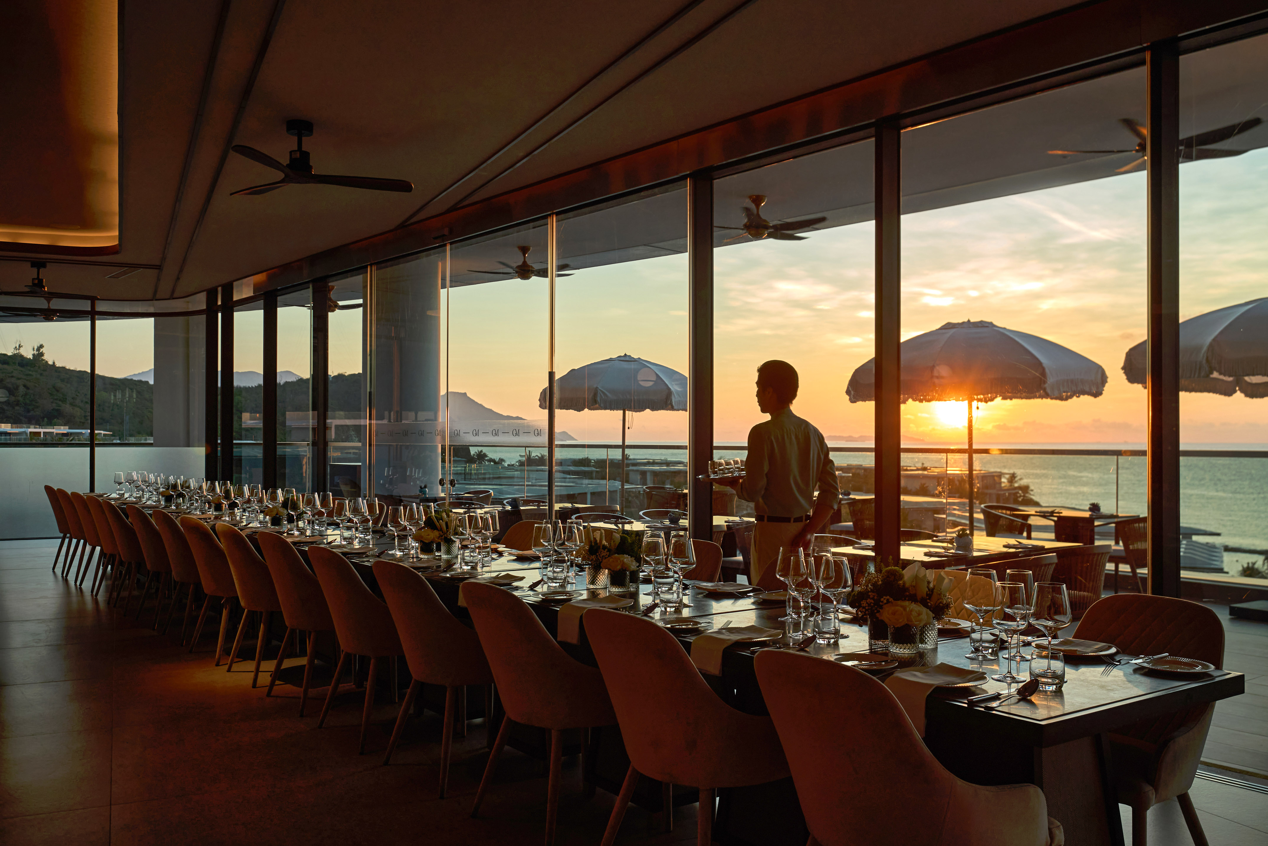 Oceanfront luxury dining room, long table set for an elegant dinner at sunset.