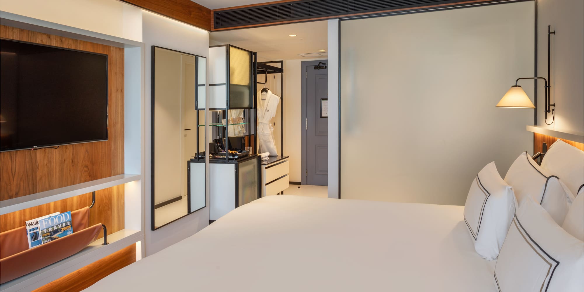 Modern hotel room with king bed, wall TV, and vanity area.