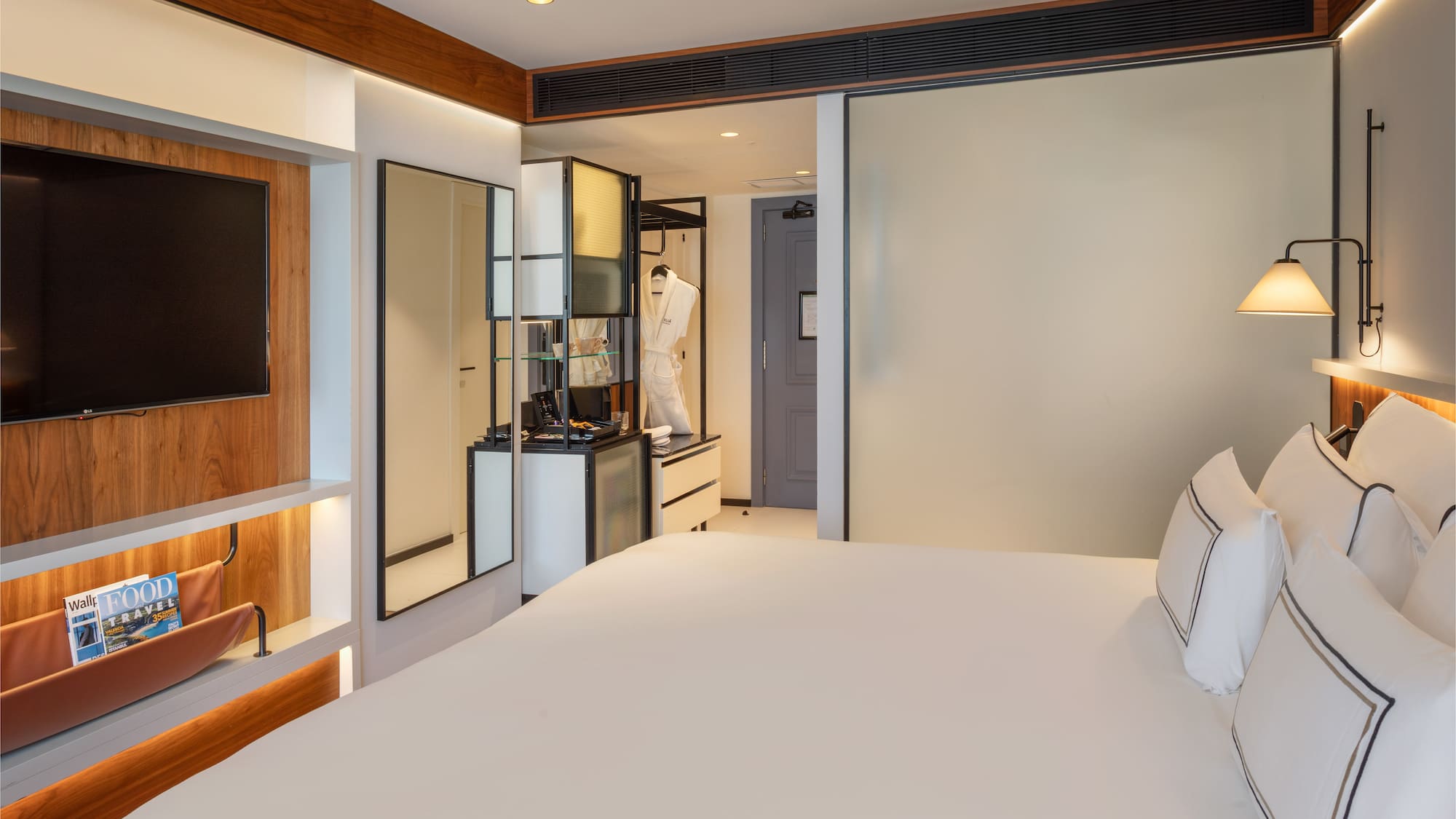 Modern hotel room with king bed, wall TV, and vanity area.