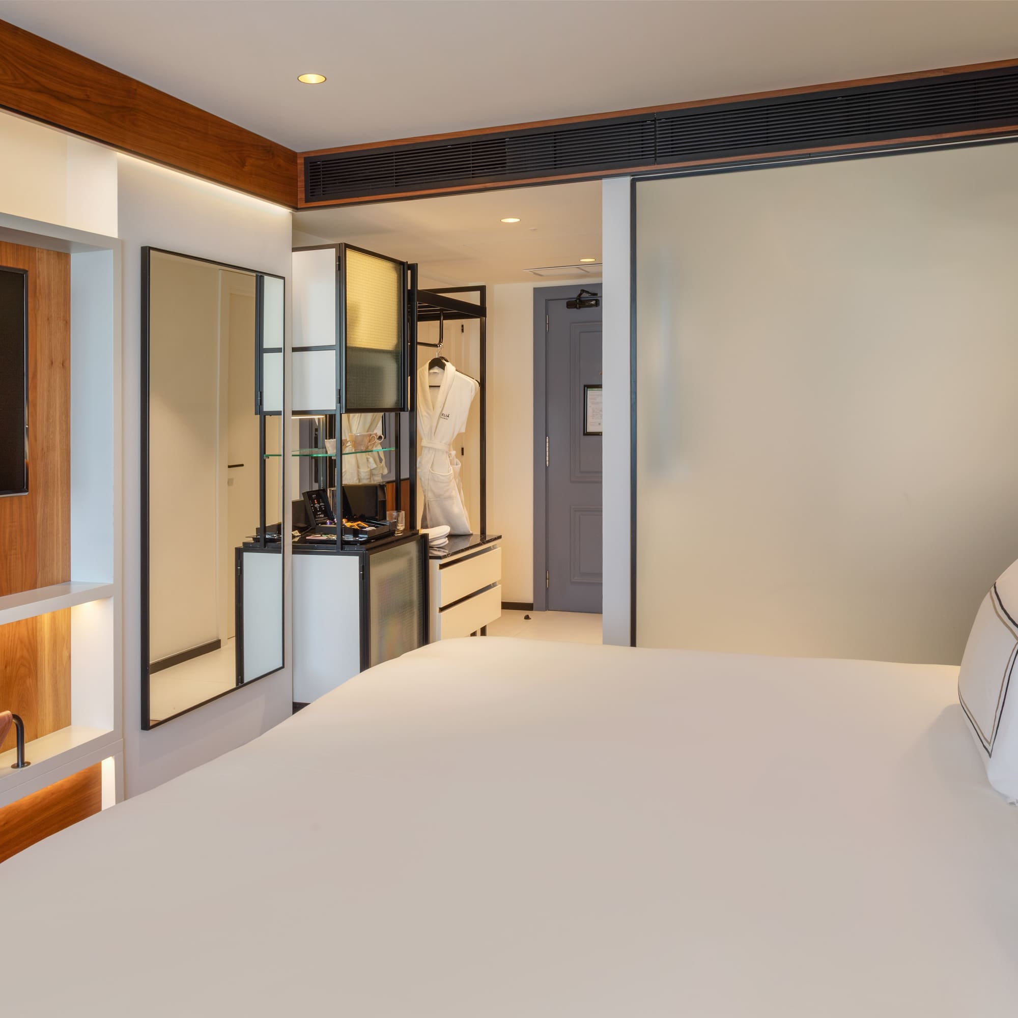 Modern hotel room with king bed, wall TV, and vanity area.