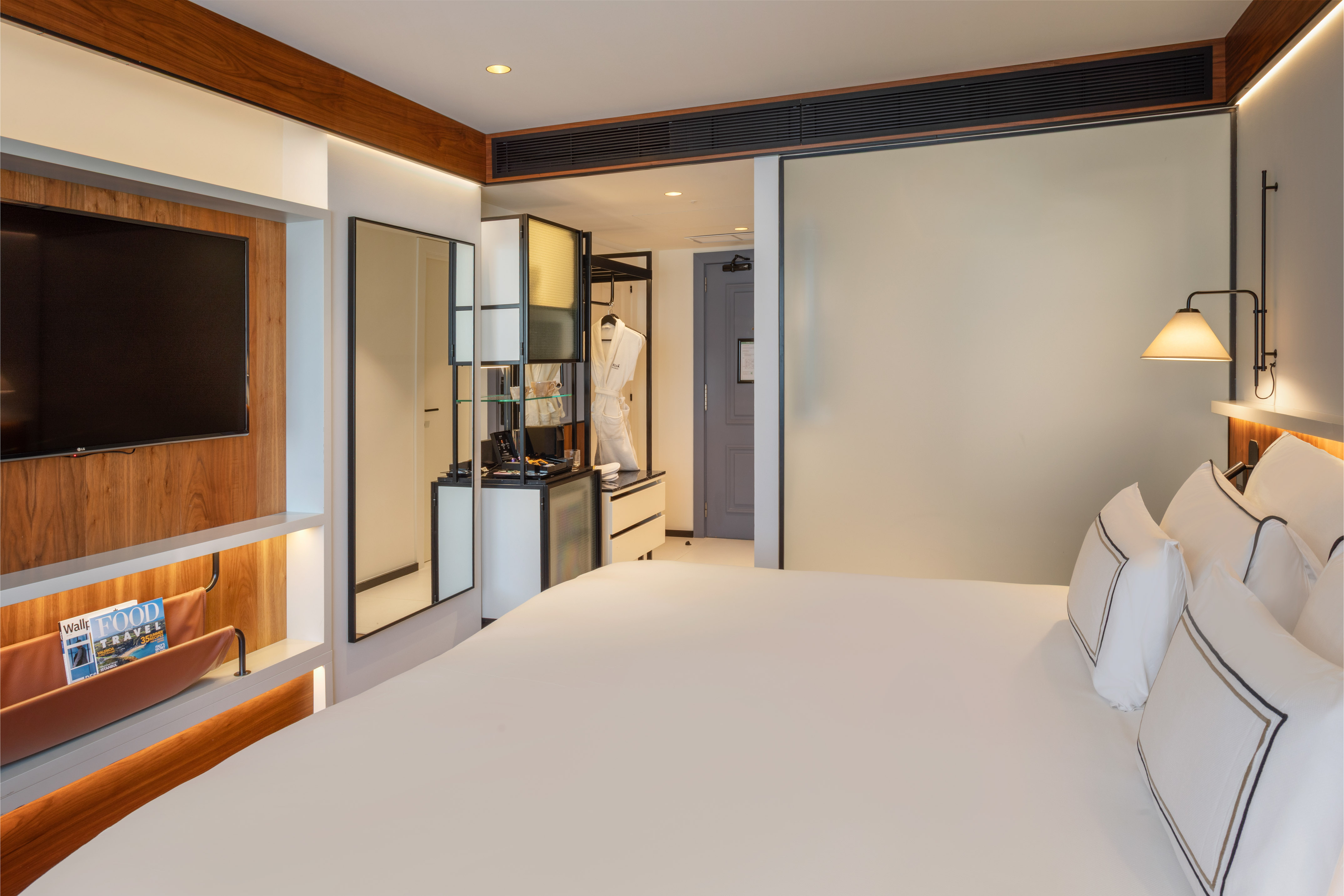 Modern hotel room with king bed, wall TV, and vanity area.