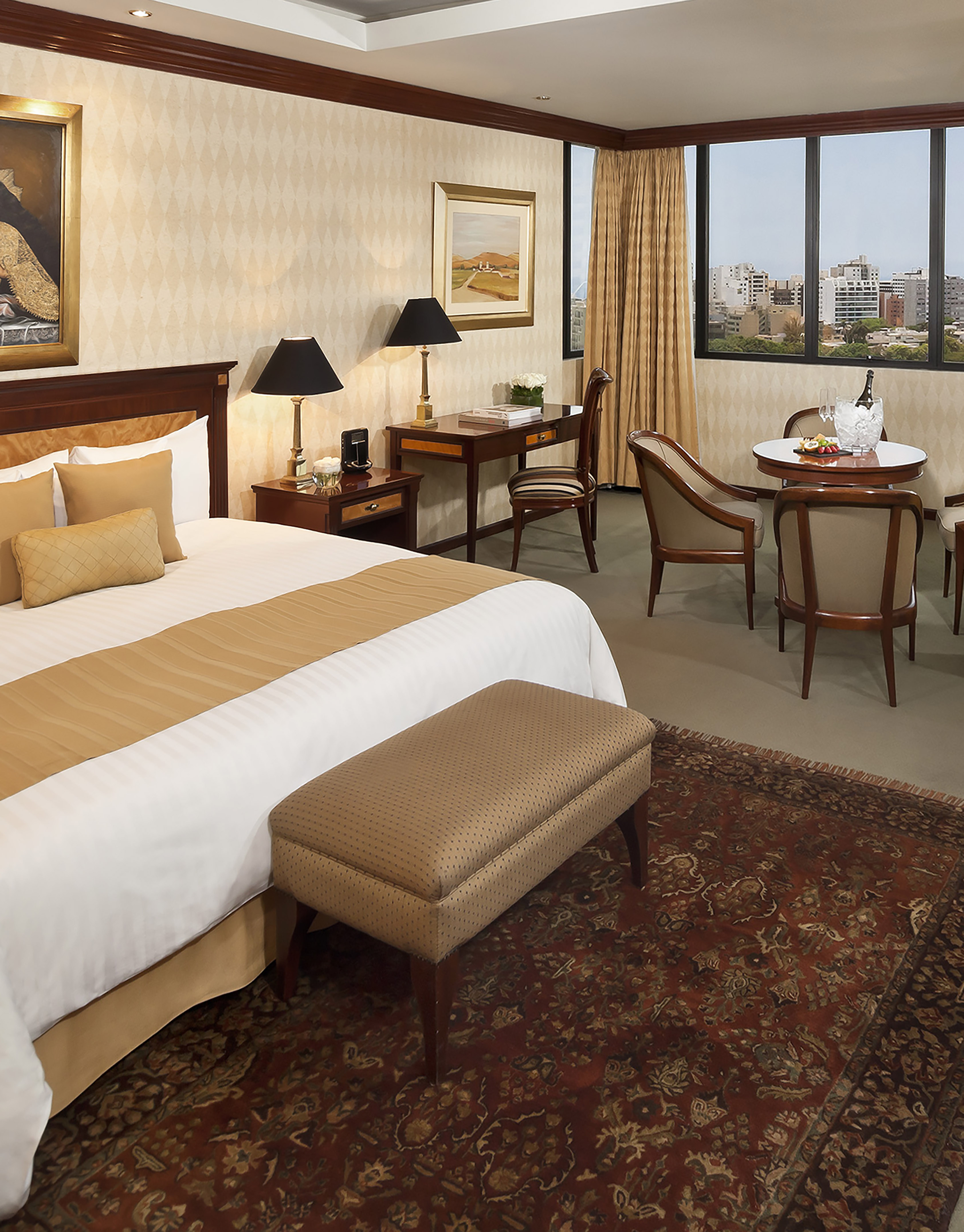 Luxurious hotel bedroom with king bed, desk, sitting area, city skyline view.