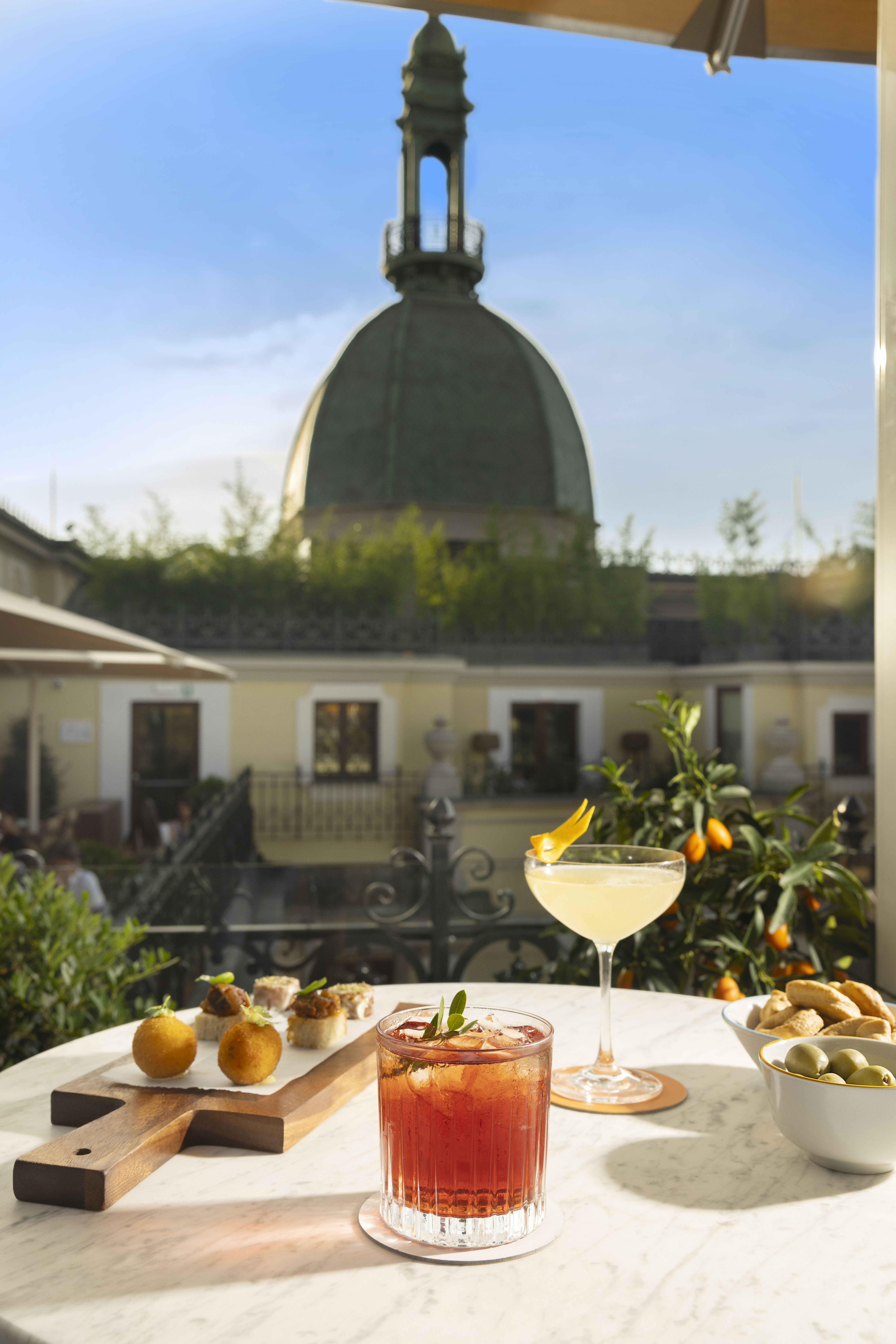 Aperitivo on a rooftop terrace with cocktails, snacks, and a city dome view.