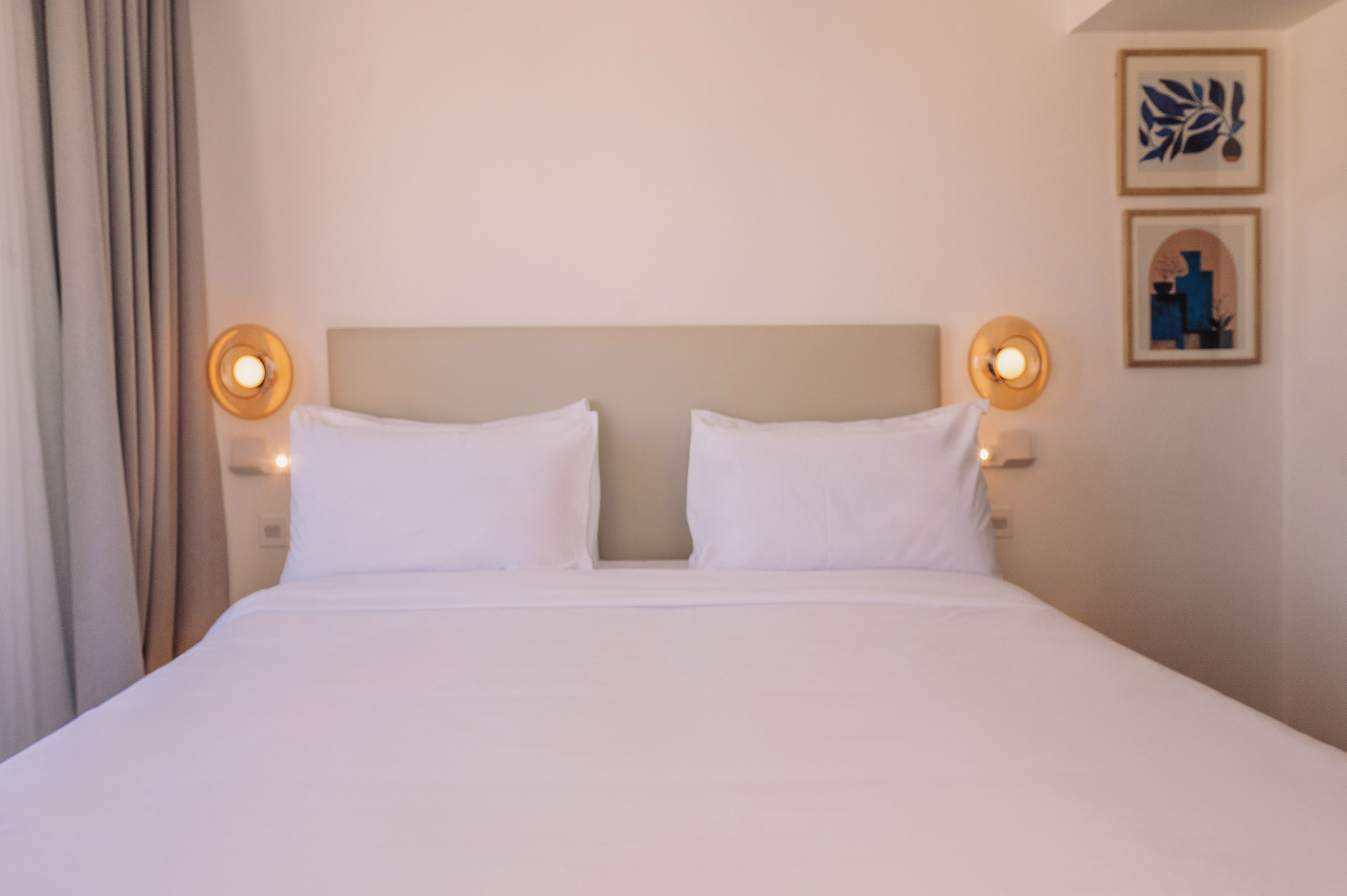 Clean white bed in a modern bedroom with beige headboard and warm bedside lamps.