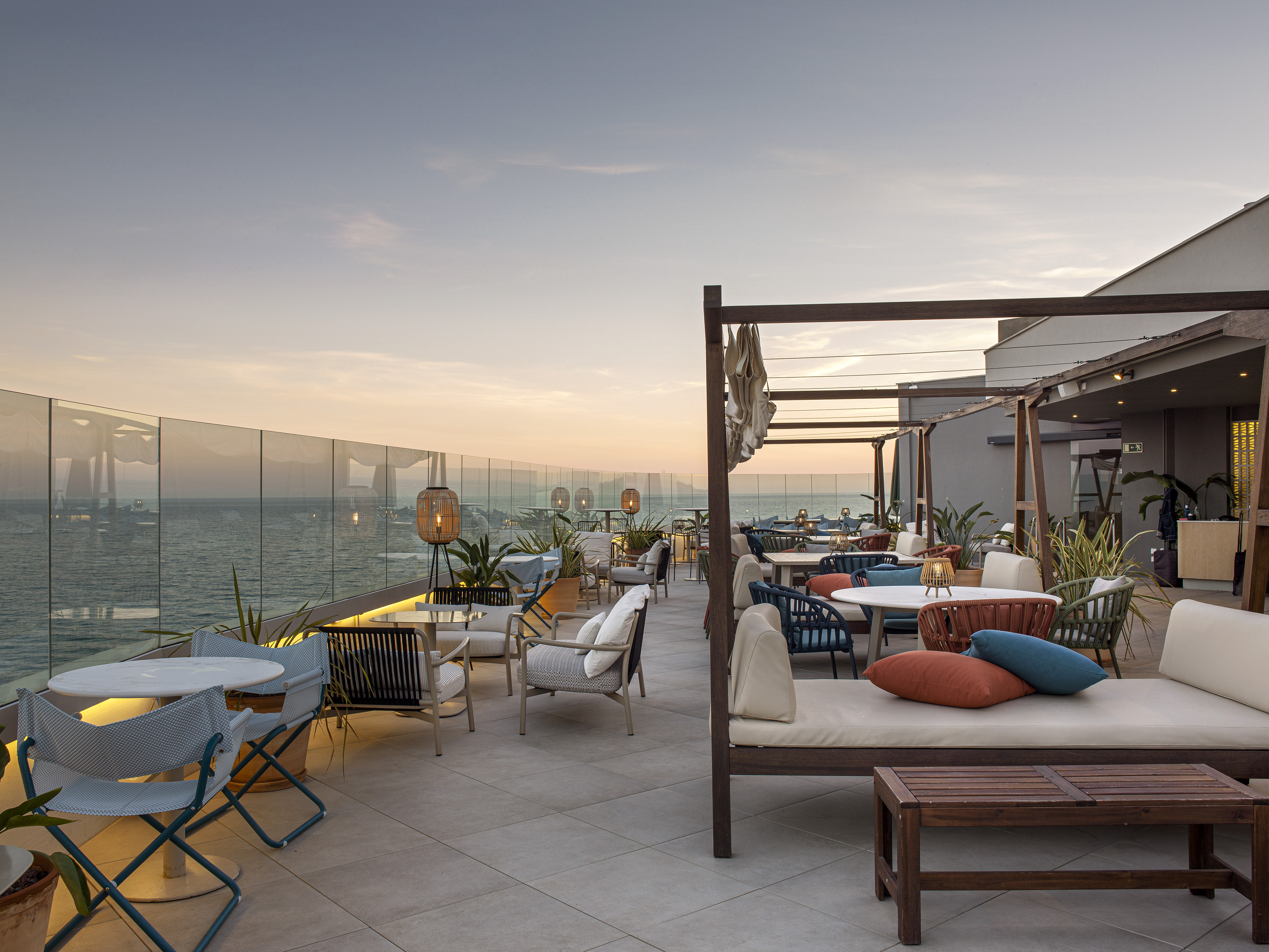 Modern rooftop ocean view lounge at sunset with stylish outdoor seating.
