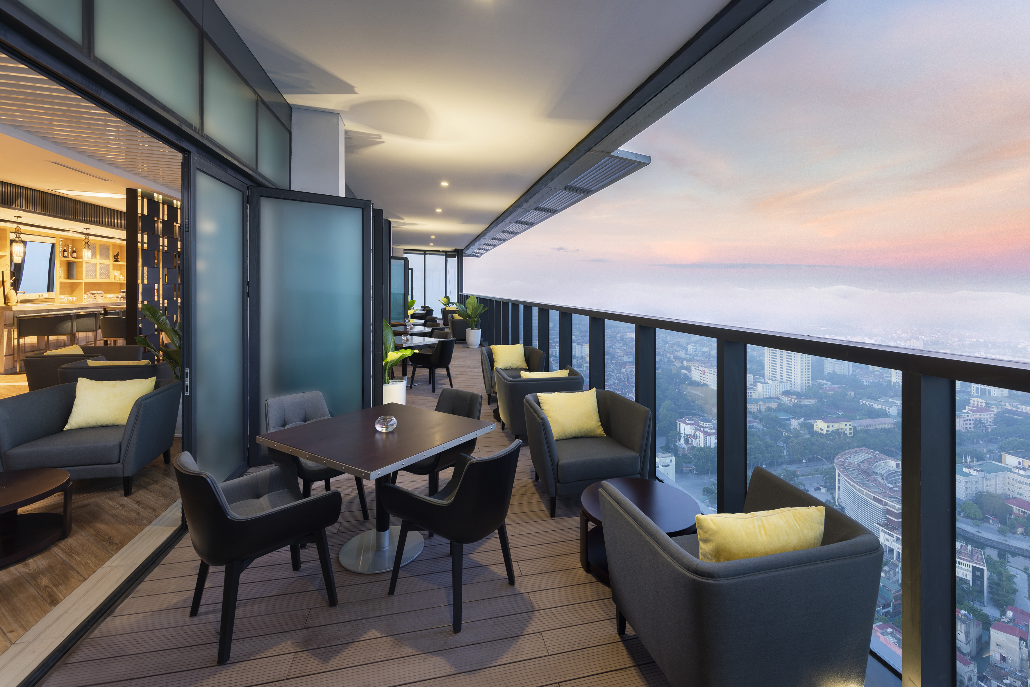 Modern rooftop lounge with comfy seating and panoramic city views at sunset.