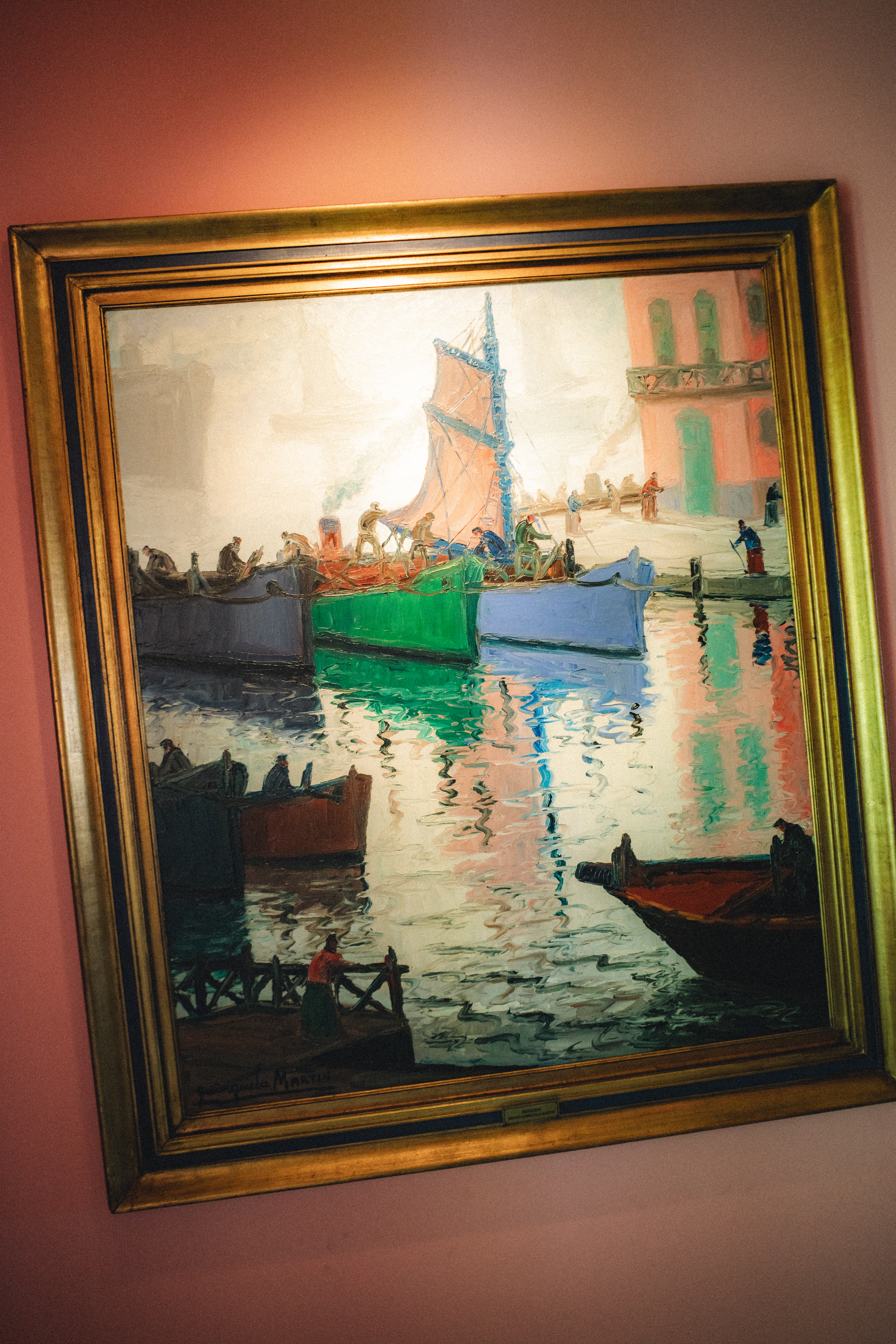 Pintura de barcos coloridos en puerto, con reflejos y marco dorado.
