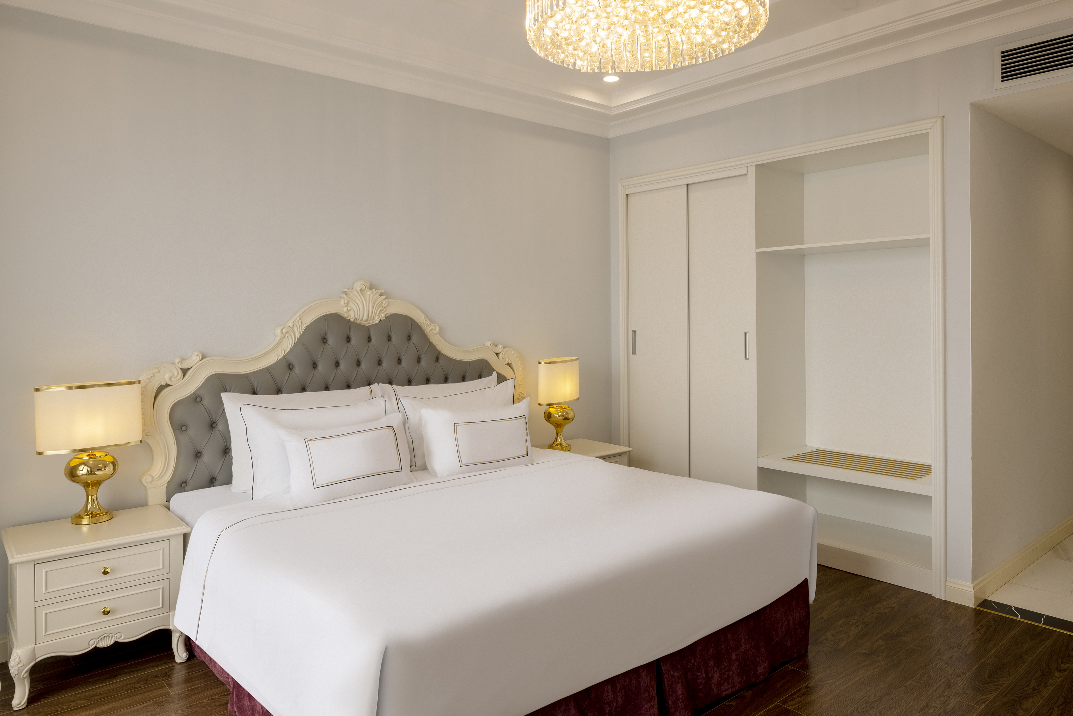 Elegant hotel bedroom with large bed, tufted headboard, and built-in closet.