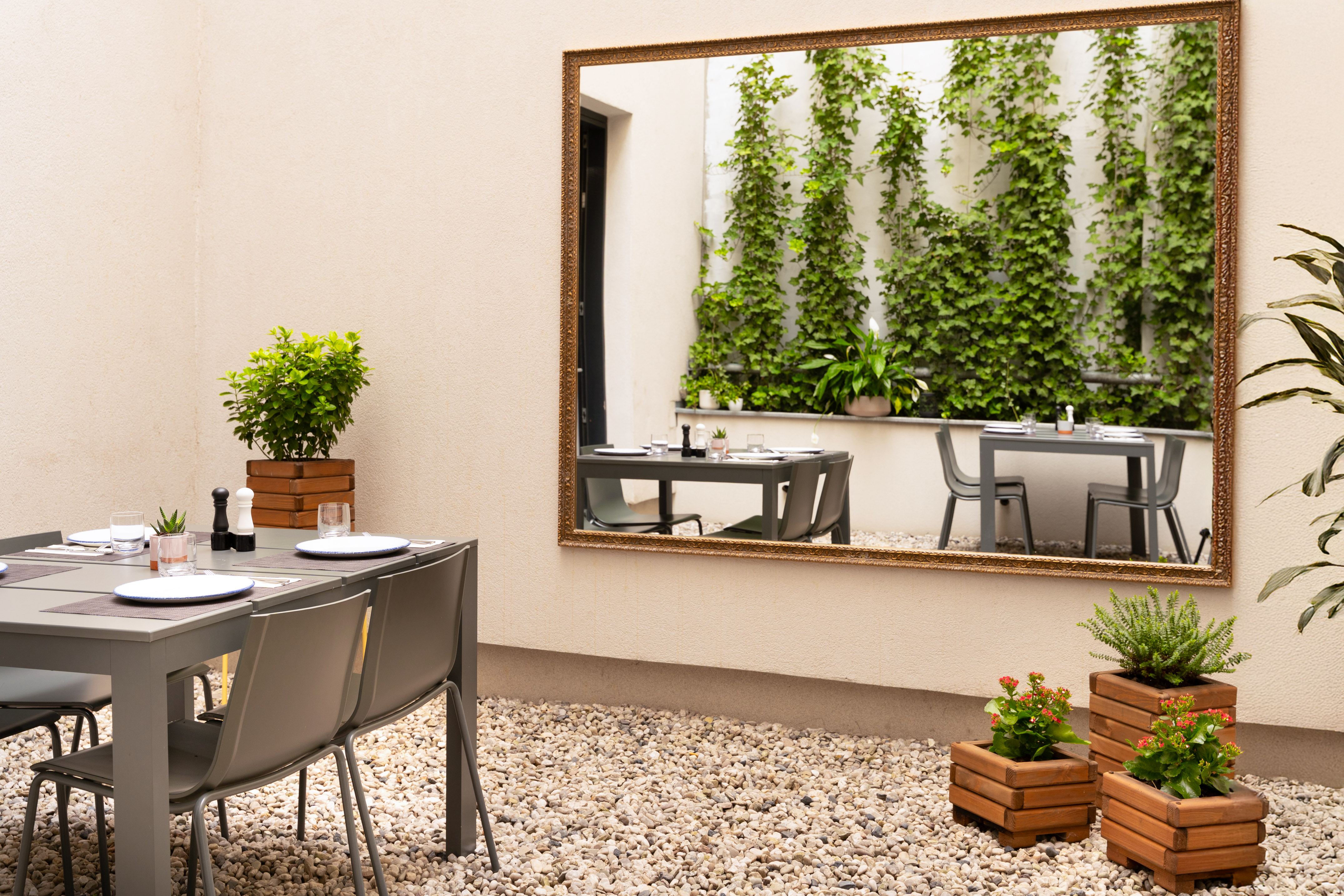 Outdoor patio dining, plants, gravel ground, mirror reflecting ivy wall.