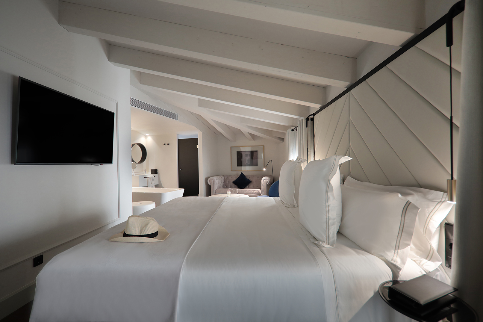Luxurious white bedroom suite with king bed, TV, and exposed ceiling beams.