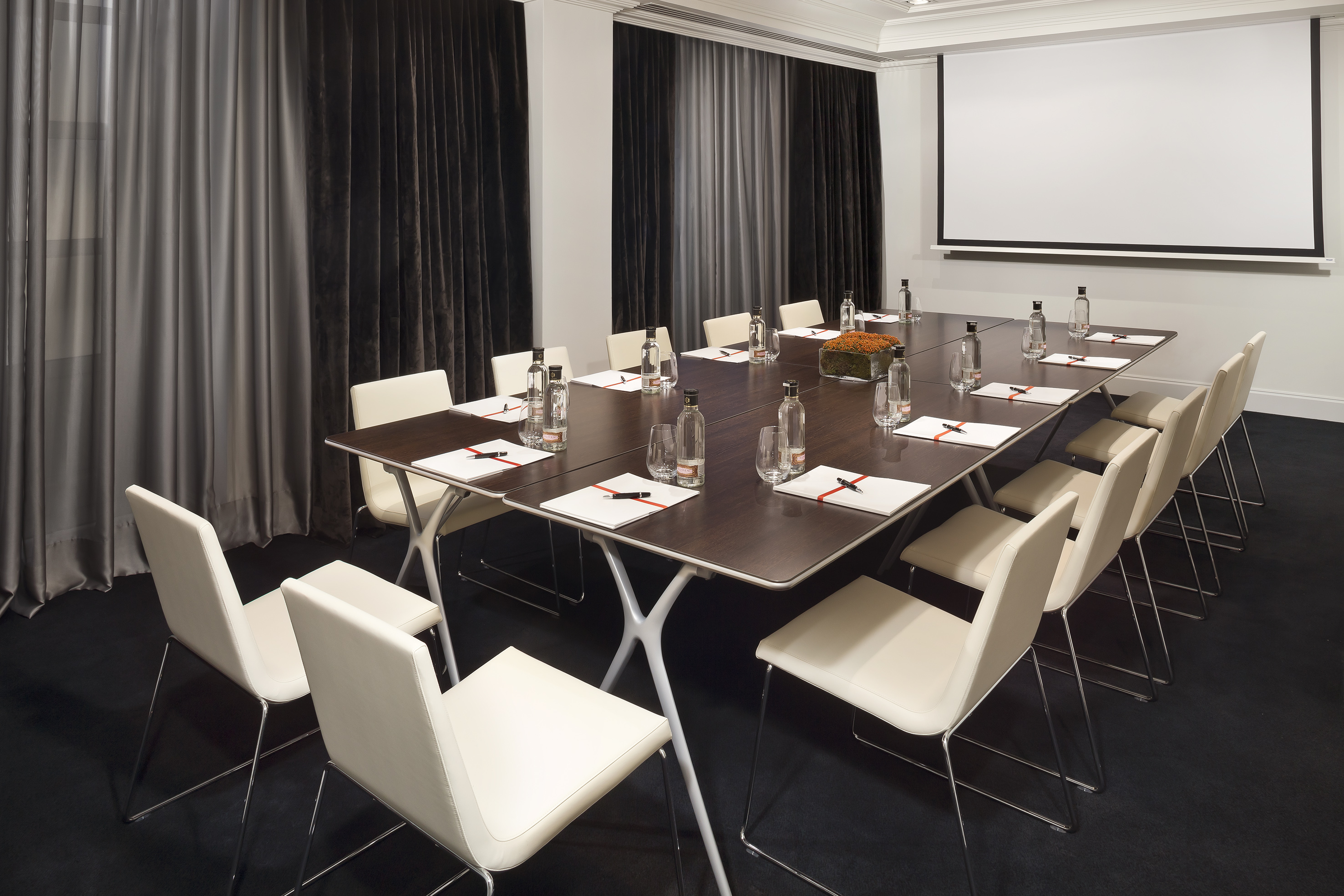Modern conference room with dark table, light chairs, and projector screen.