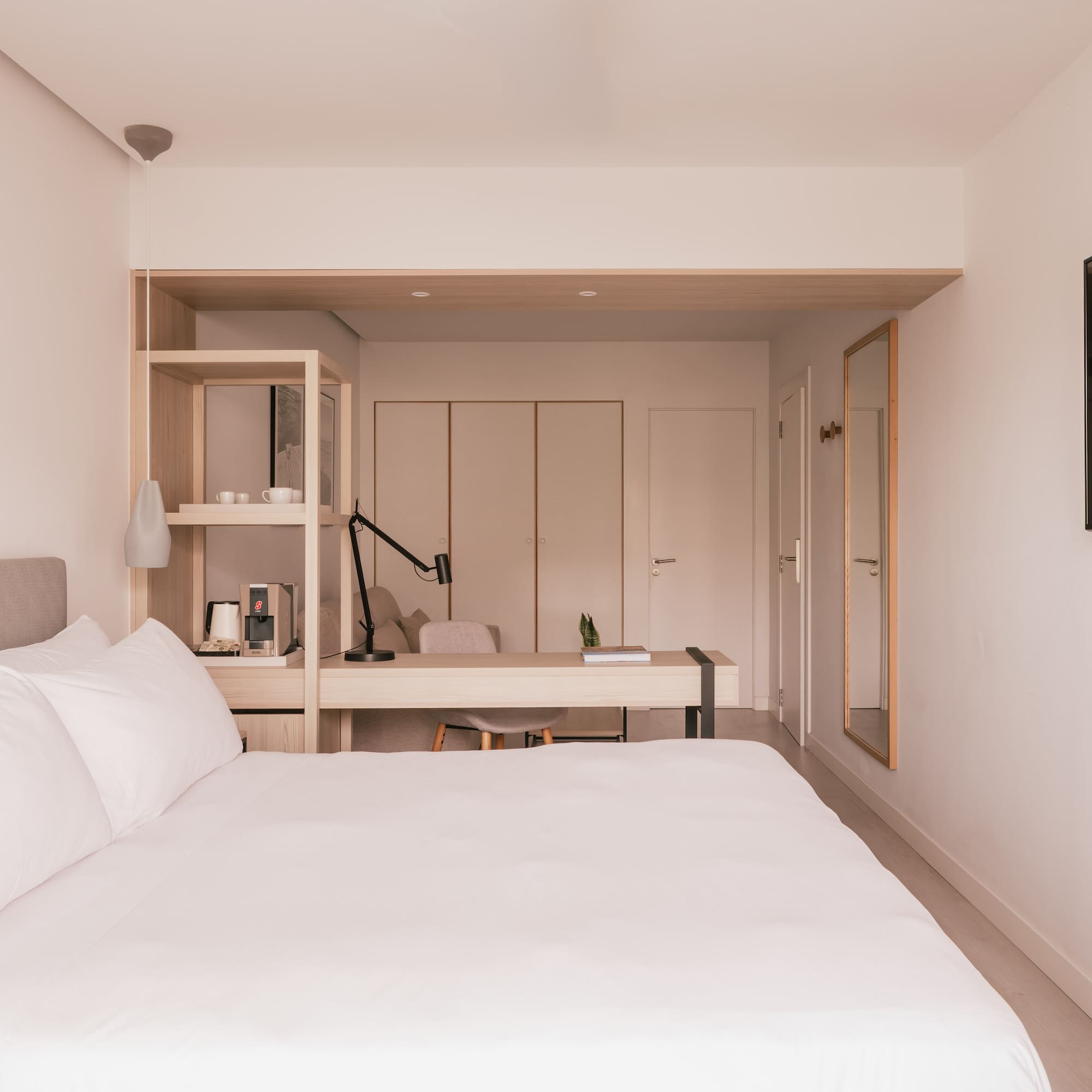 Modern hotel bedroom with white bed, desk, TV, and coffee station.