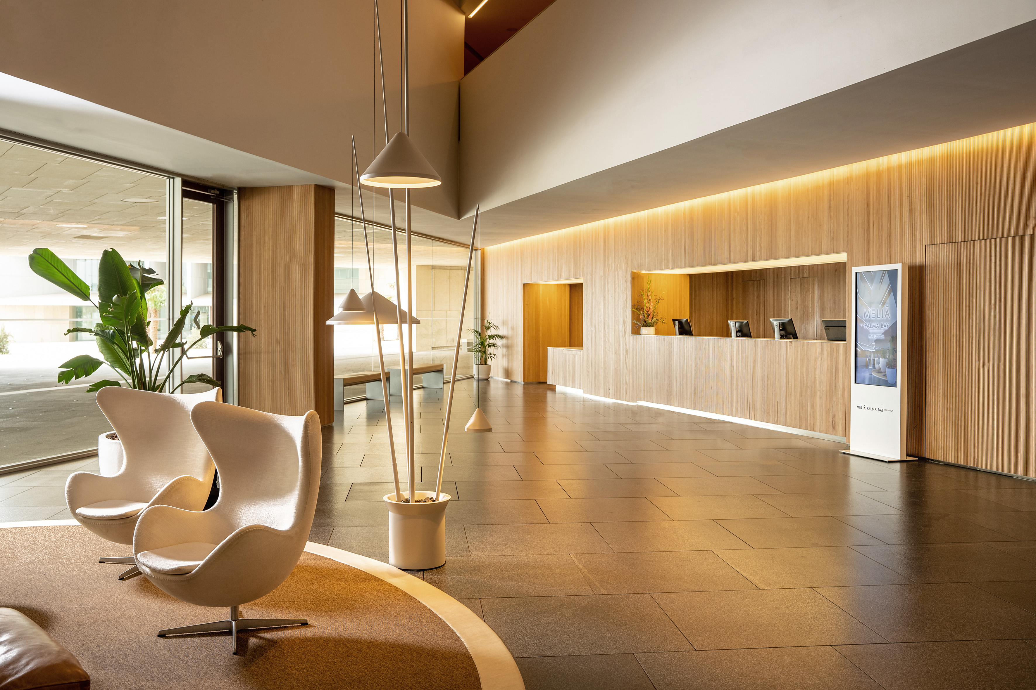 Melia hotel lobby: modern wood paneling, reception desk, and white Egg chairs.