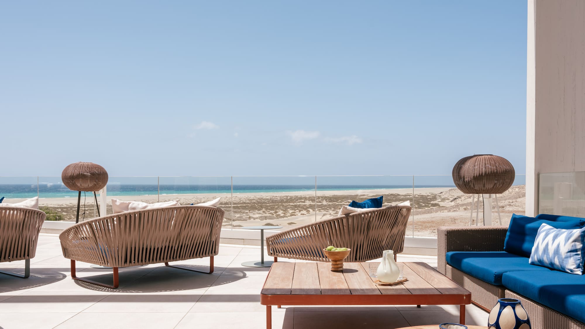 Sunny outdoor terrace with modern lounge furniture and panoramic ocean view.