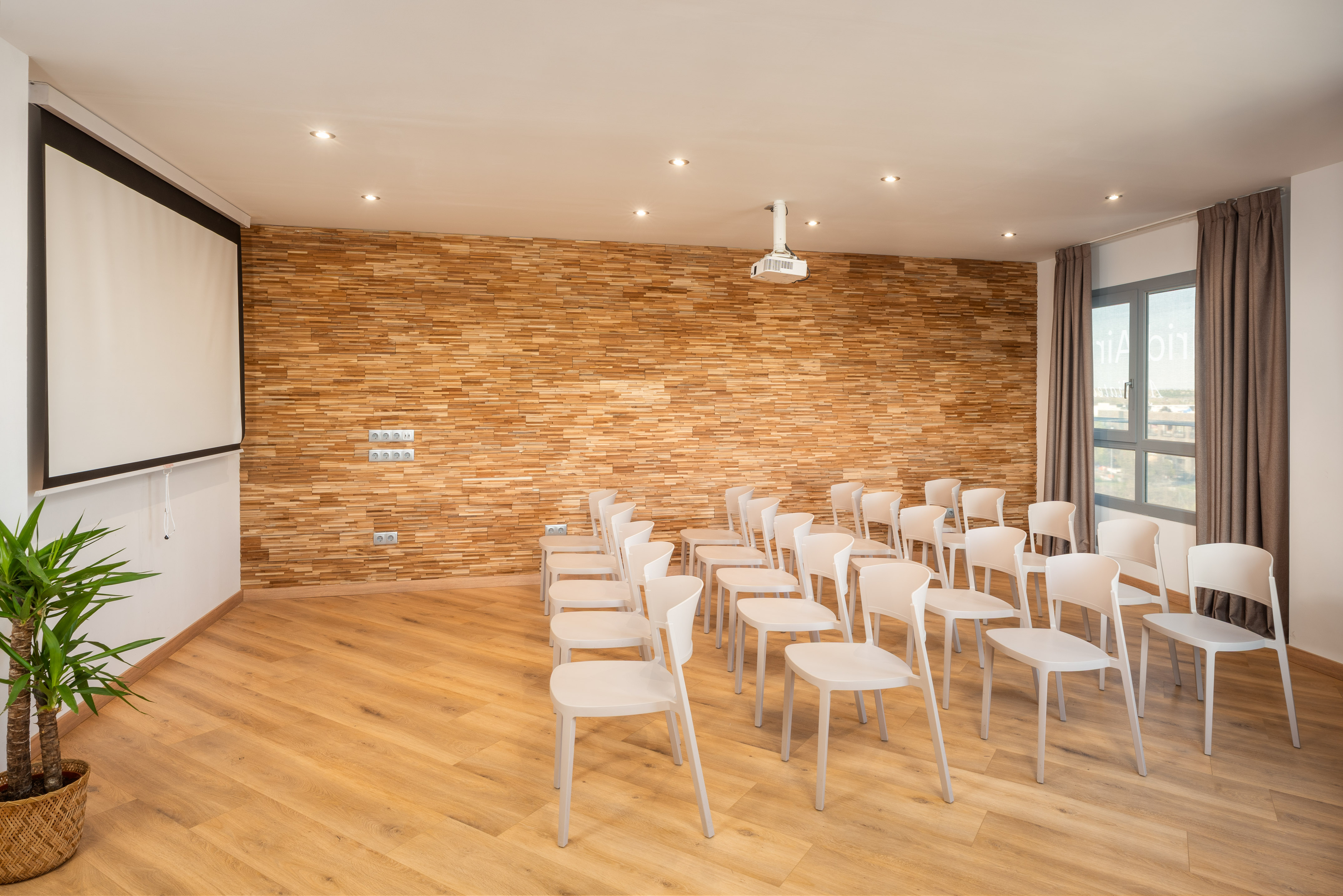 Modern conference room with projector, screen, white chairs, and wood accent wall.