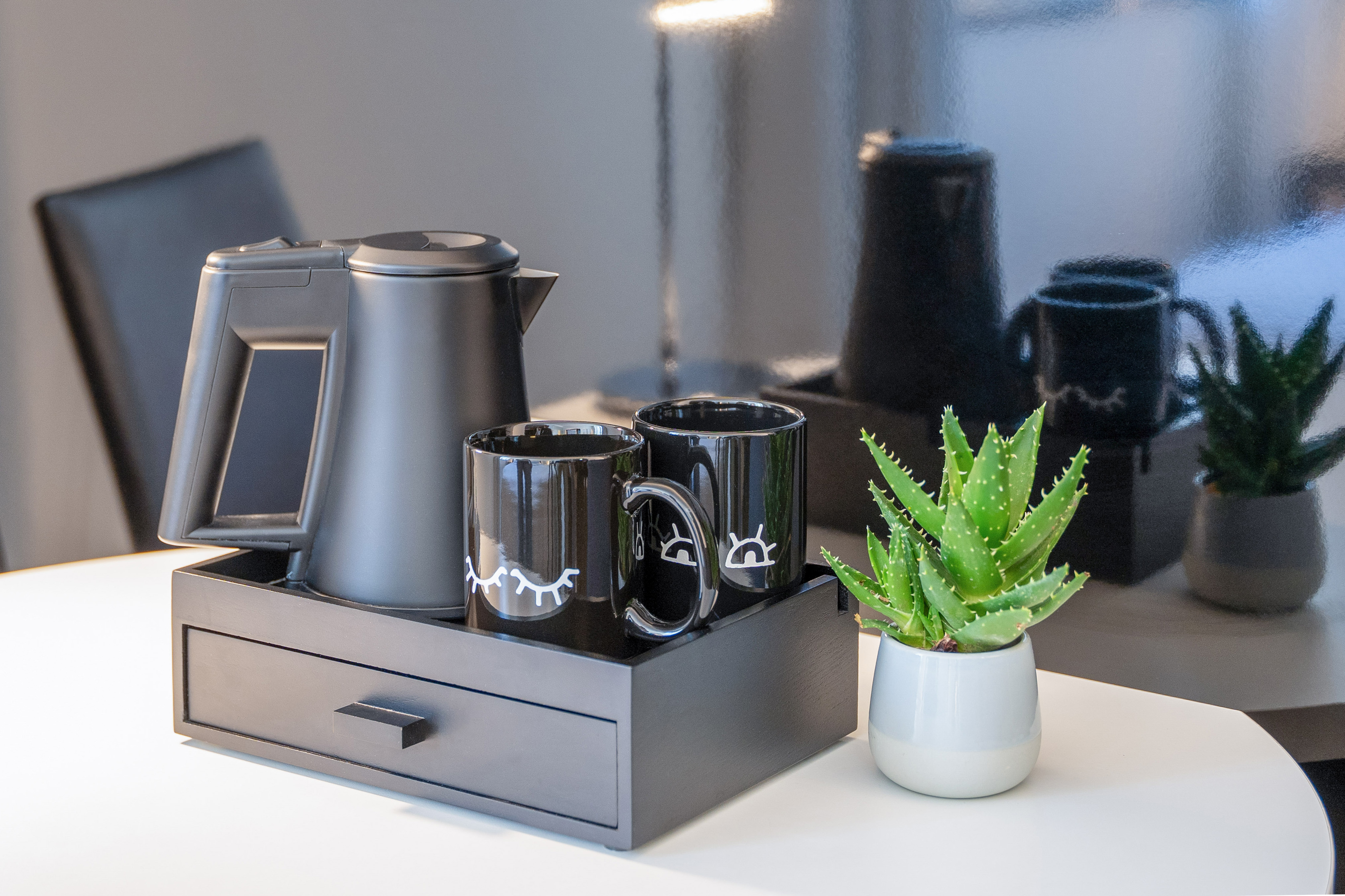 Black electric kettle, two mugs, and succulent on a modern tray.