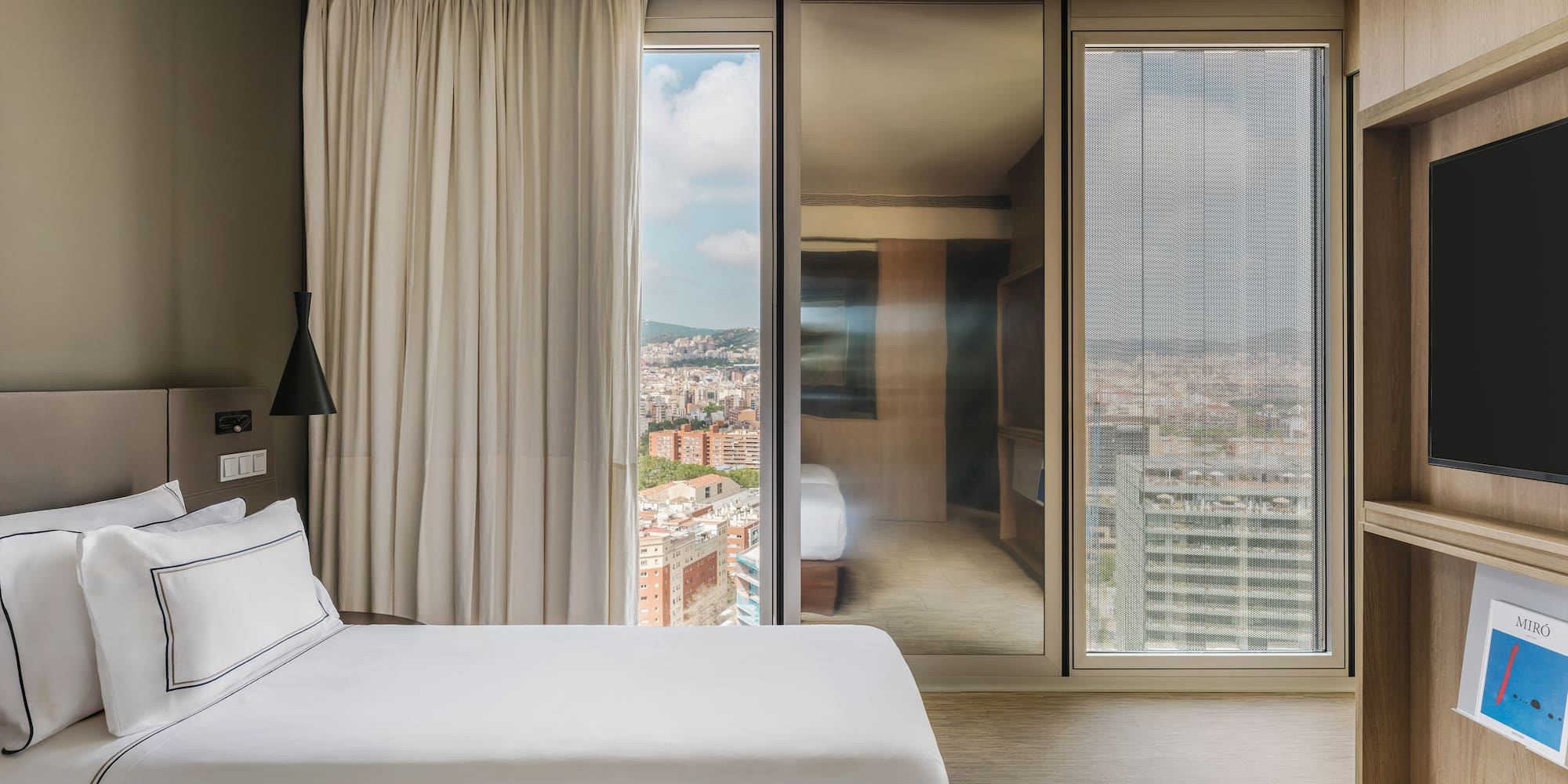 Modern hotel room with twin beds and a large window view of Barcelona city.
