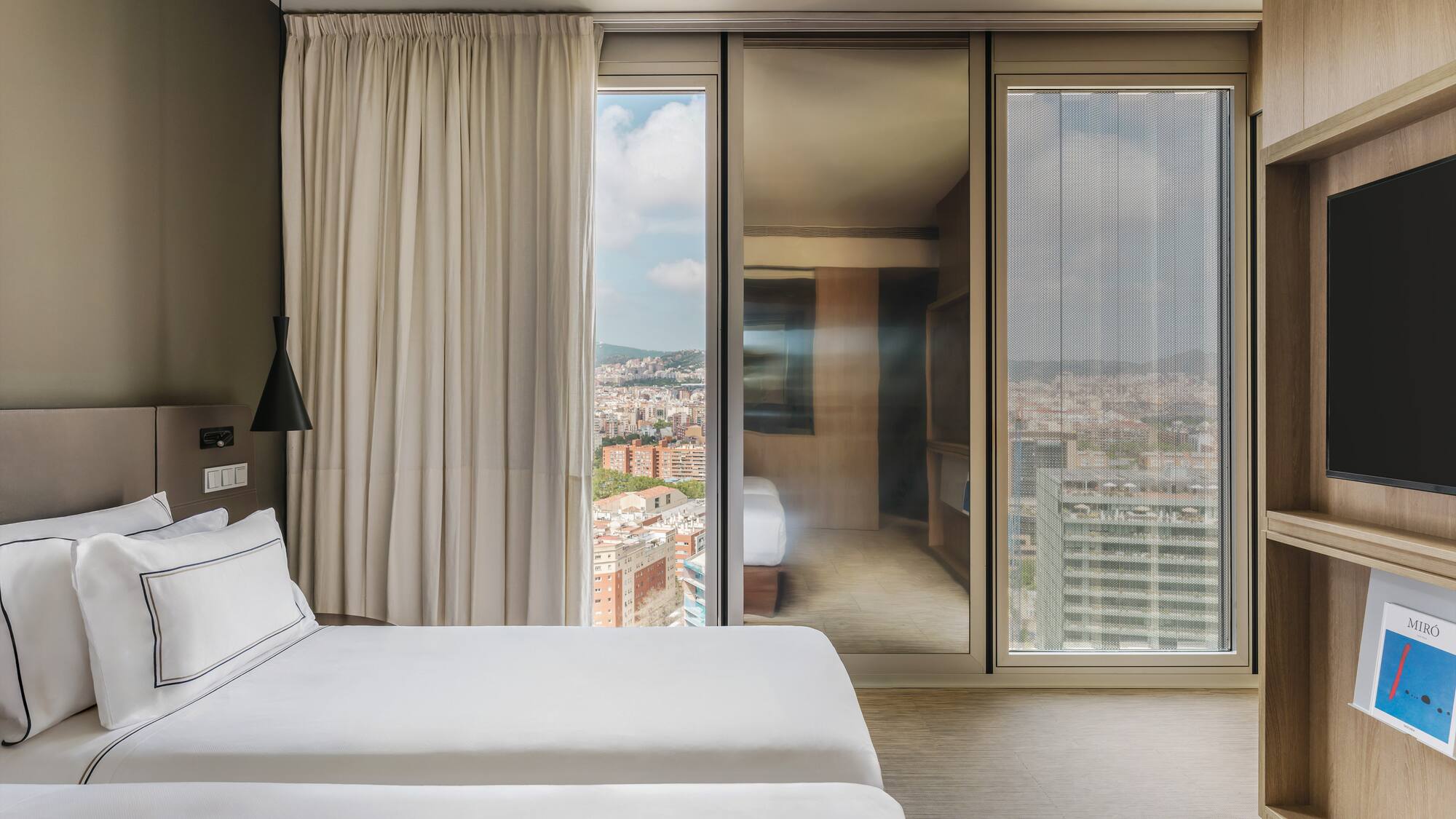 Moderna habitación de hotel con dos camas, ventanal y vistas urbanas.