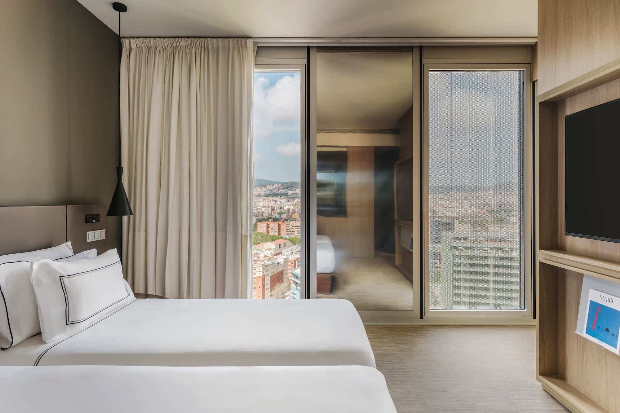 Moderna habitación de hotel con dos camas, ventanal y vistas urbanas.