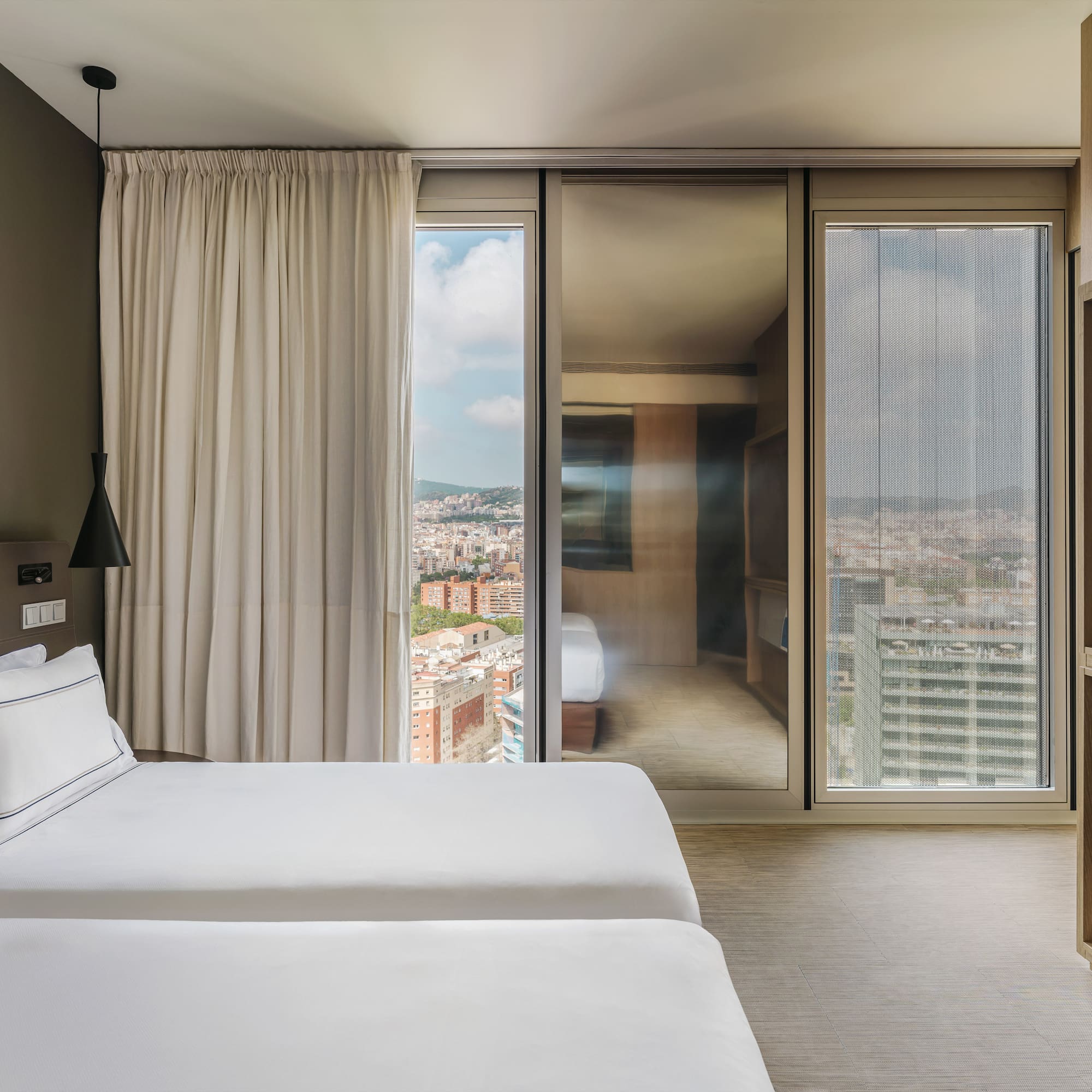 Modern hotel room with twin beds and a large window view of Barcelona city.