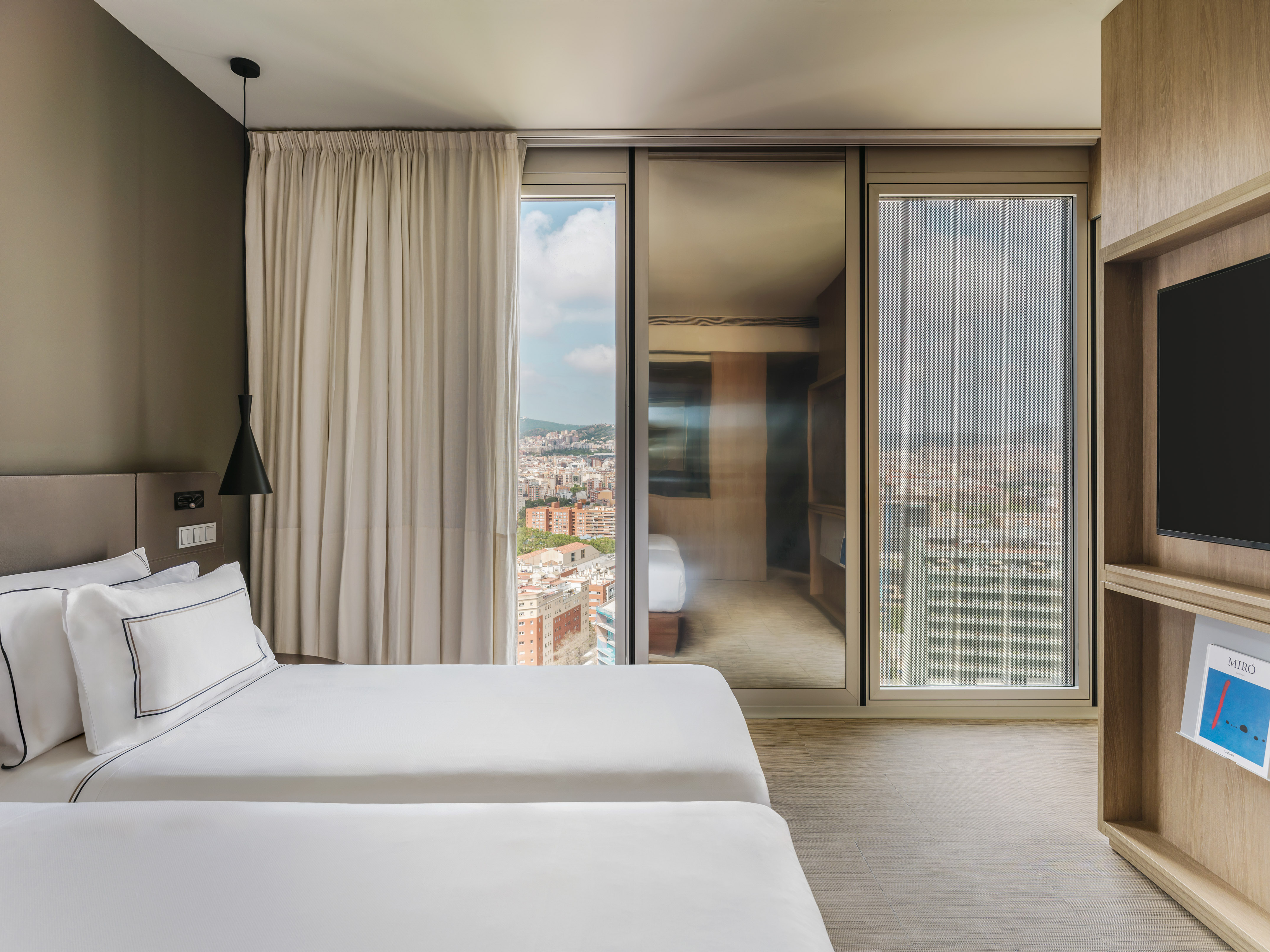 Moderna habitación de hotel con dos camas, ventanal y vistas urbanas.