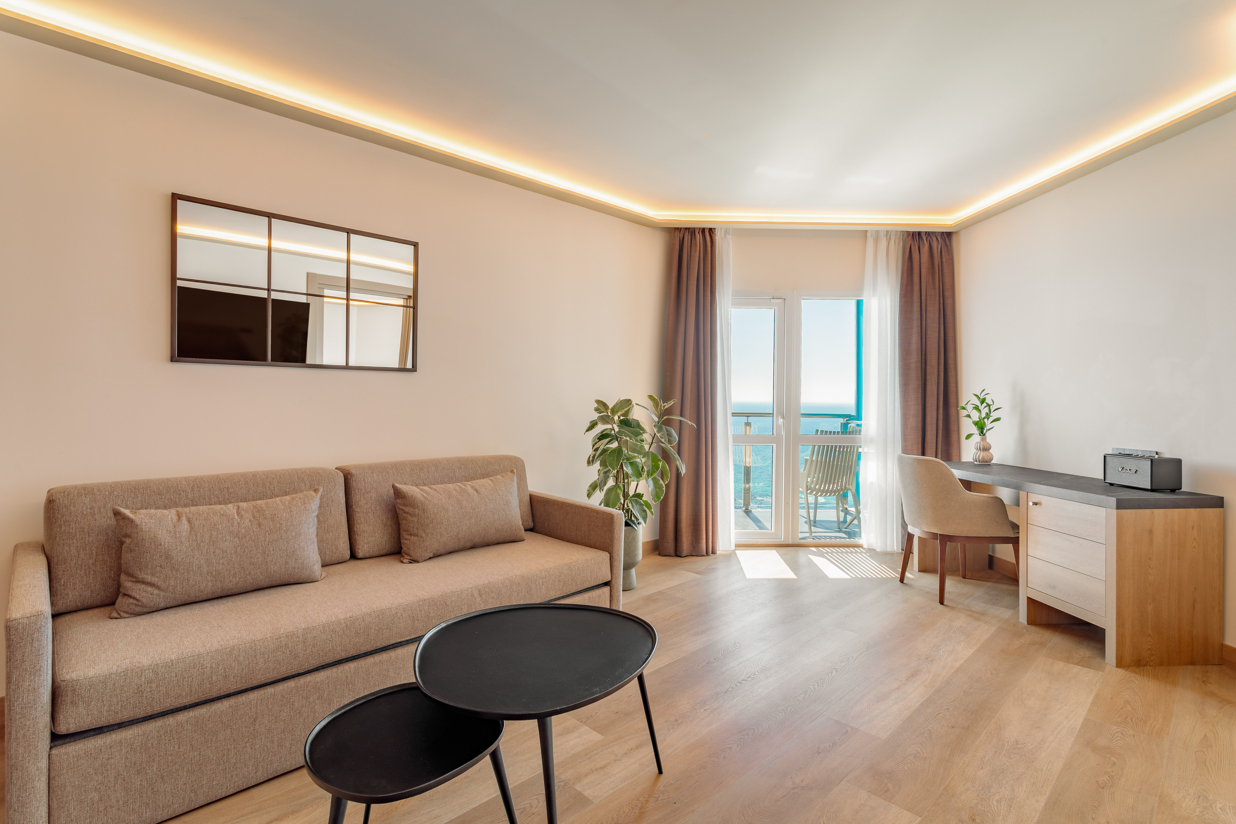 Coastal living room suite with sofa, desk, and balcony overlooking the sea.