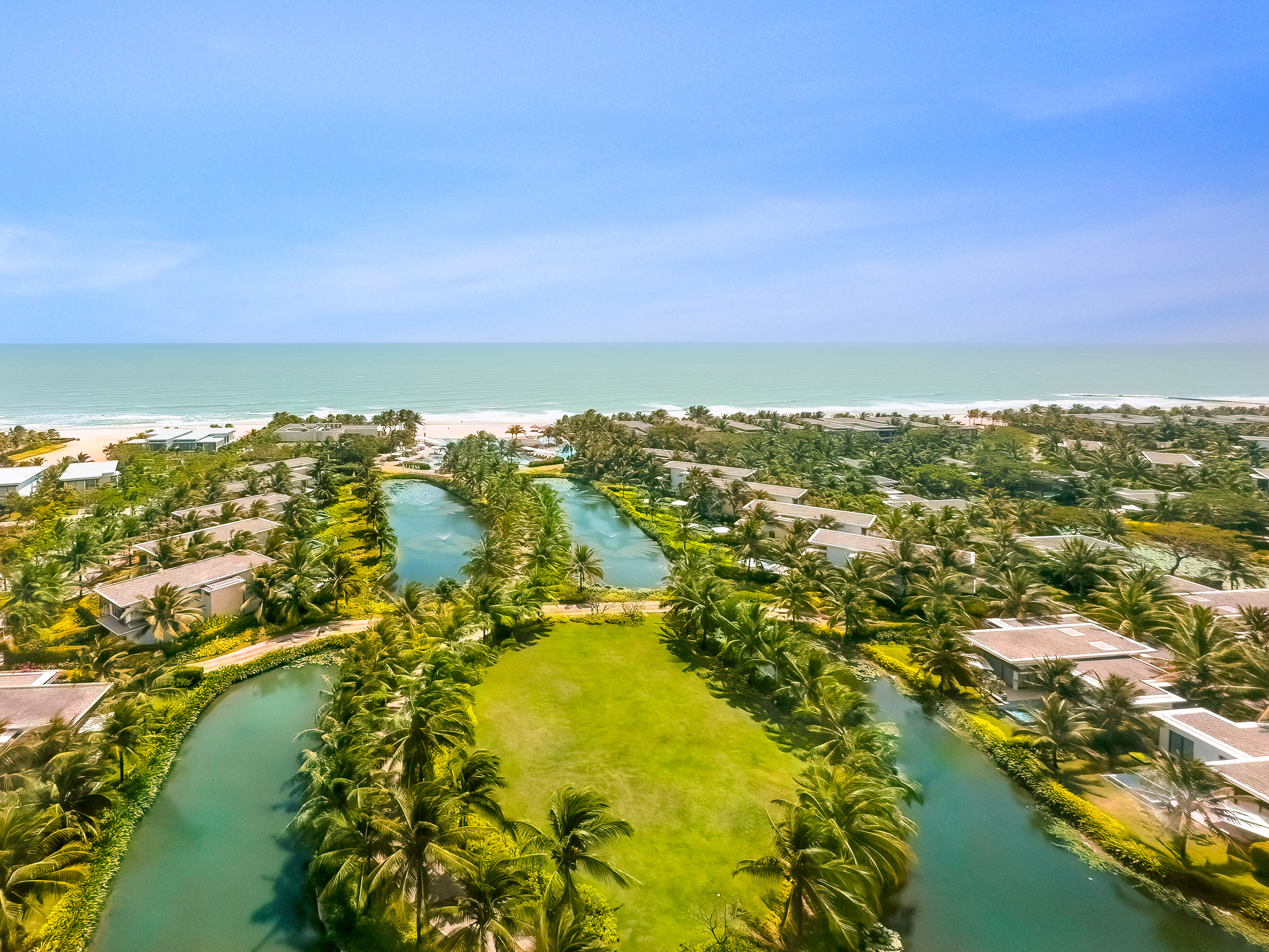 Aerial view: luxury beachfront resort, villas, palm trees, waterways.