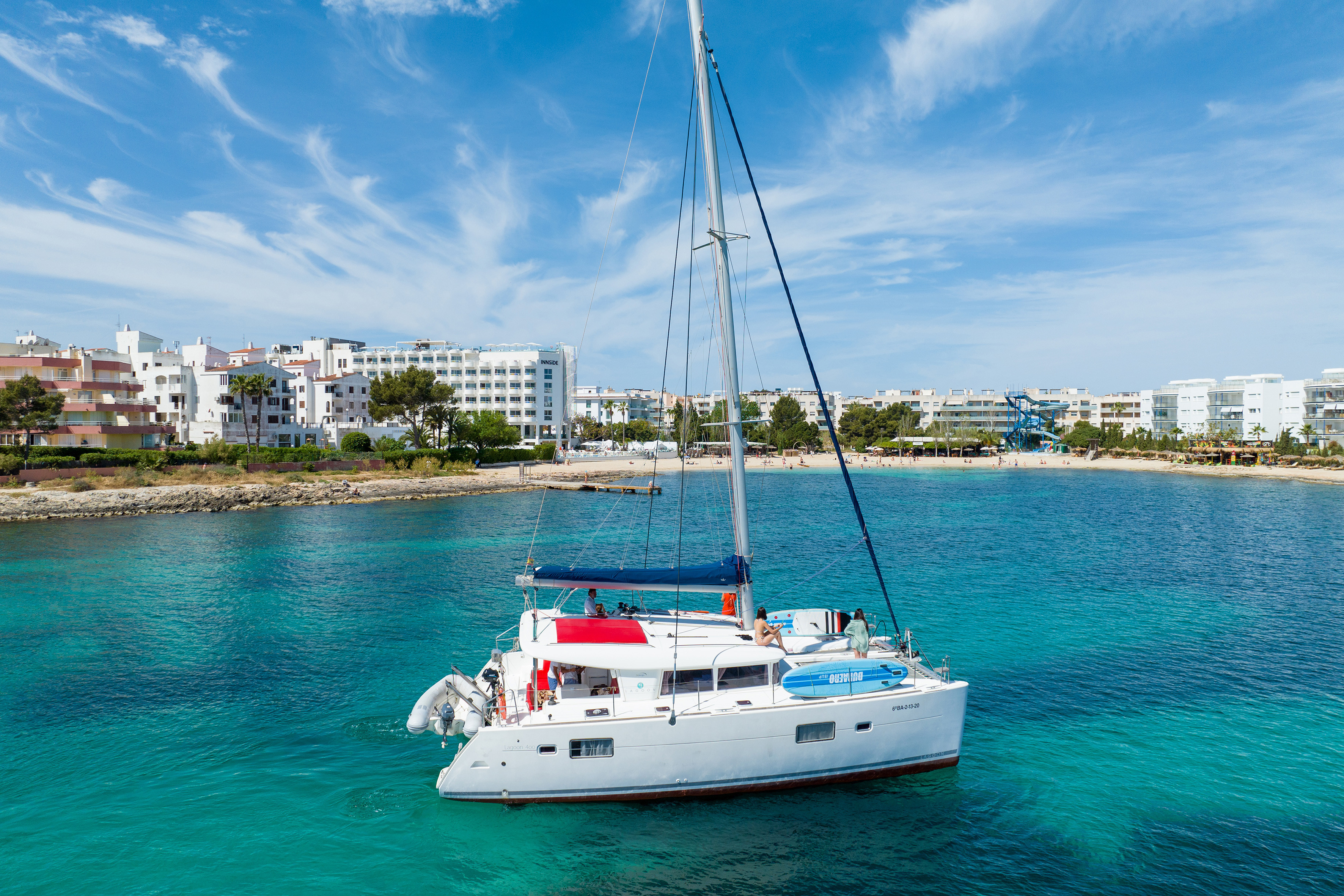 Catamaran anchored in clear turquoise water off a sunny resort beach.