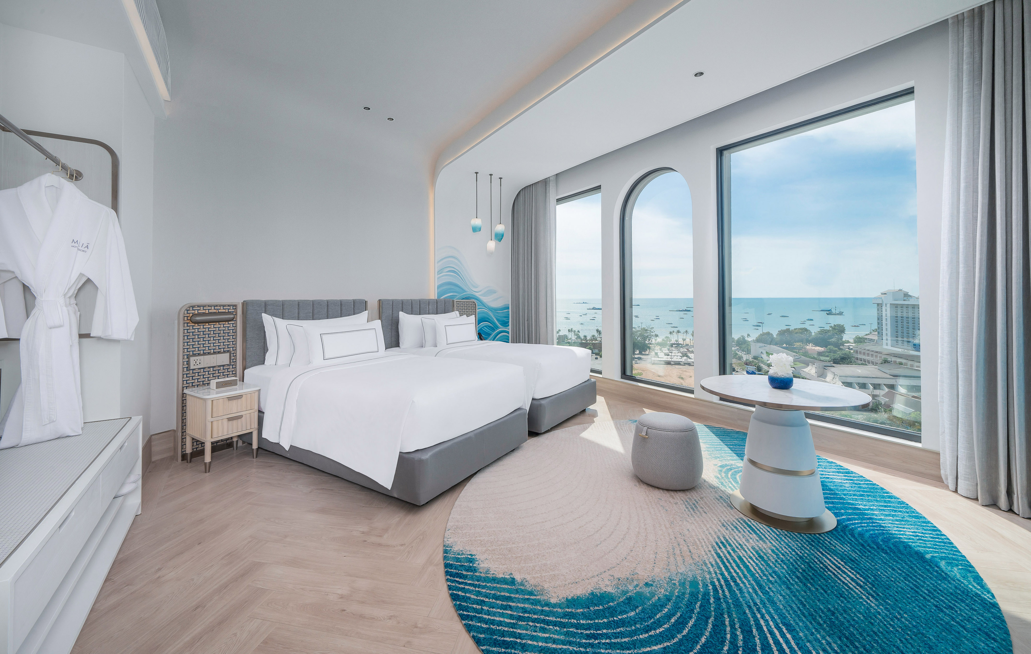 Modern hotel room, twin beds, panoramic sea view, blue wave rug.