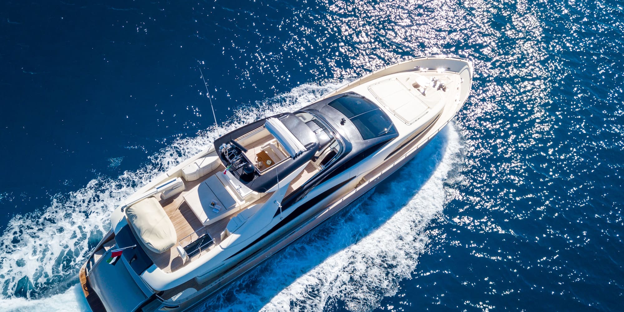 Luxury motor yacht cruising on sparkling blue ocean, aerial view.