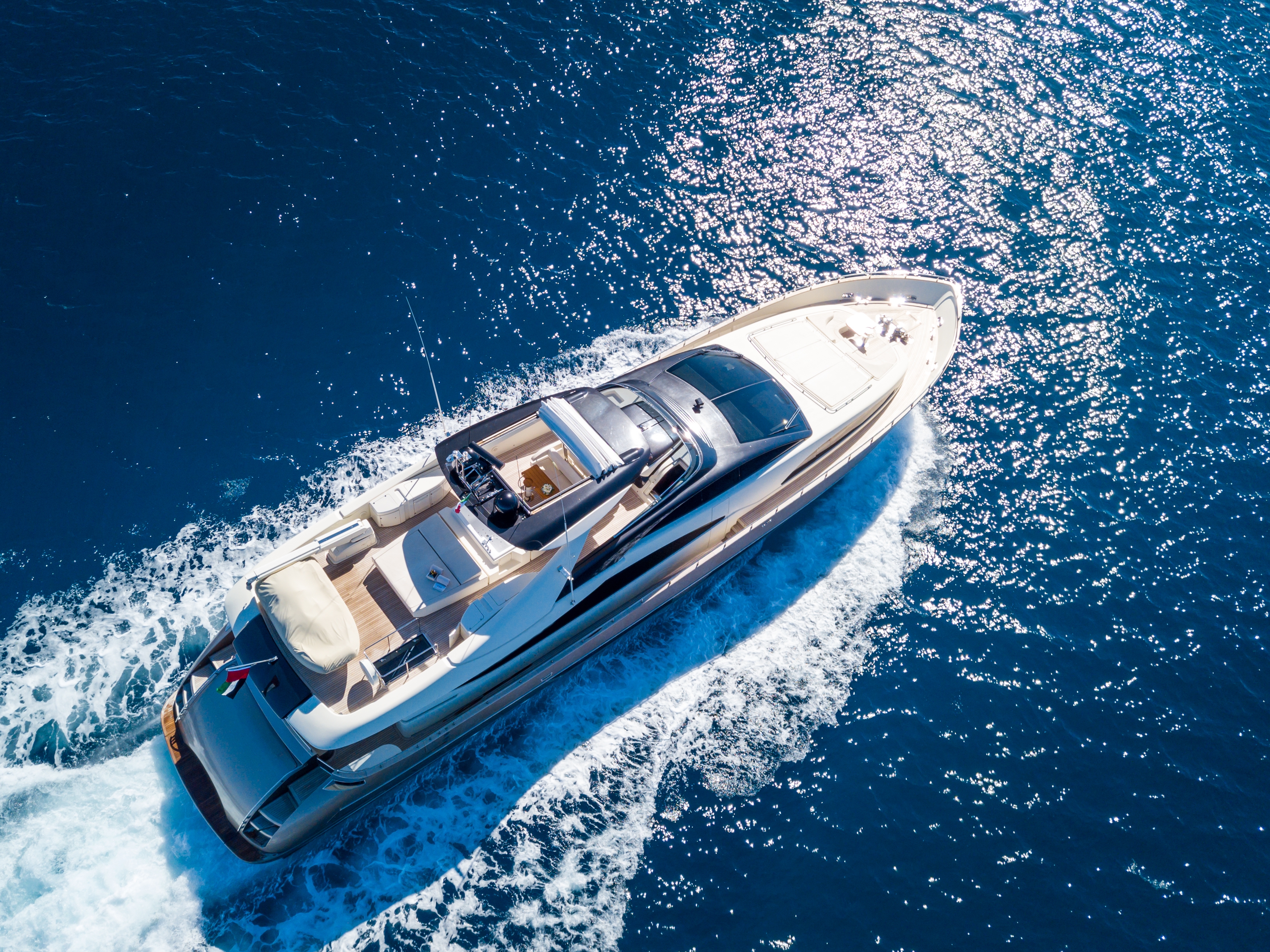 Luxury motor yacht cruising on sparkling blue ocean, aerial view.