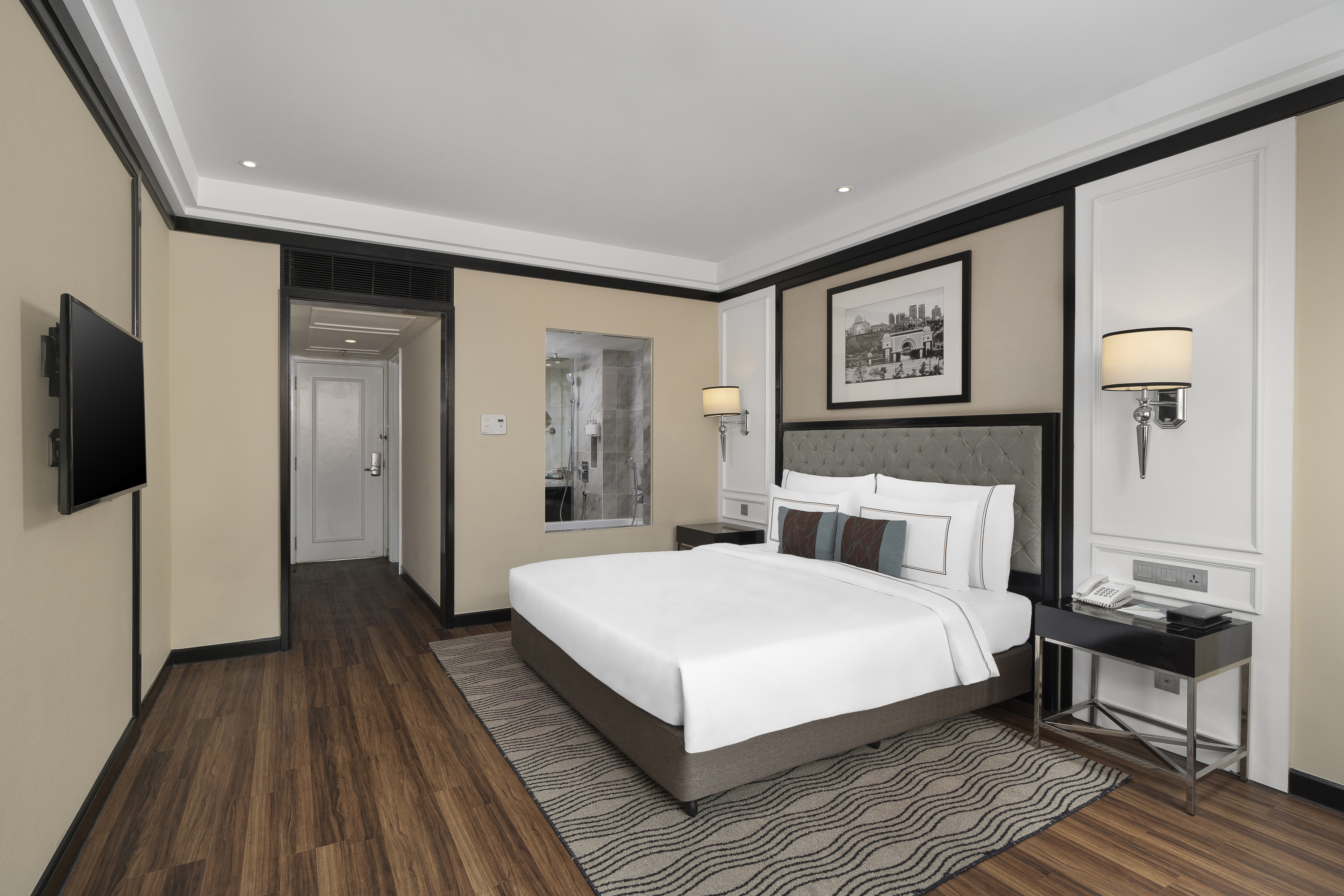 Modern hotel bedroom with king bed, wood floor, mounted TV, and visible bathroom.