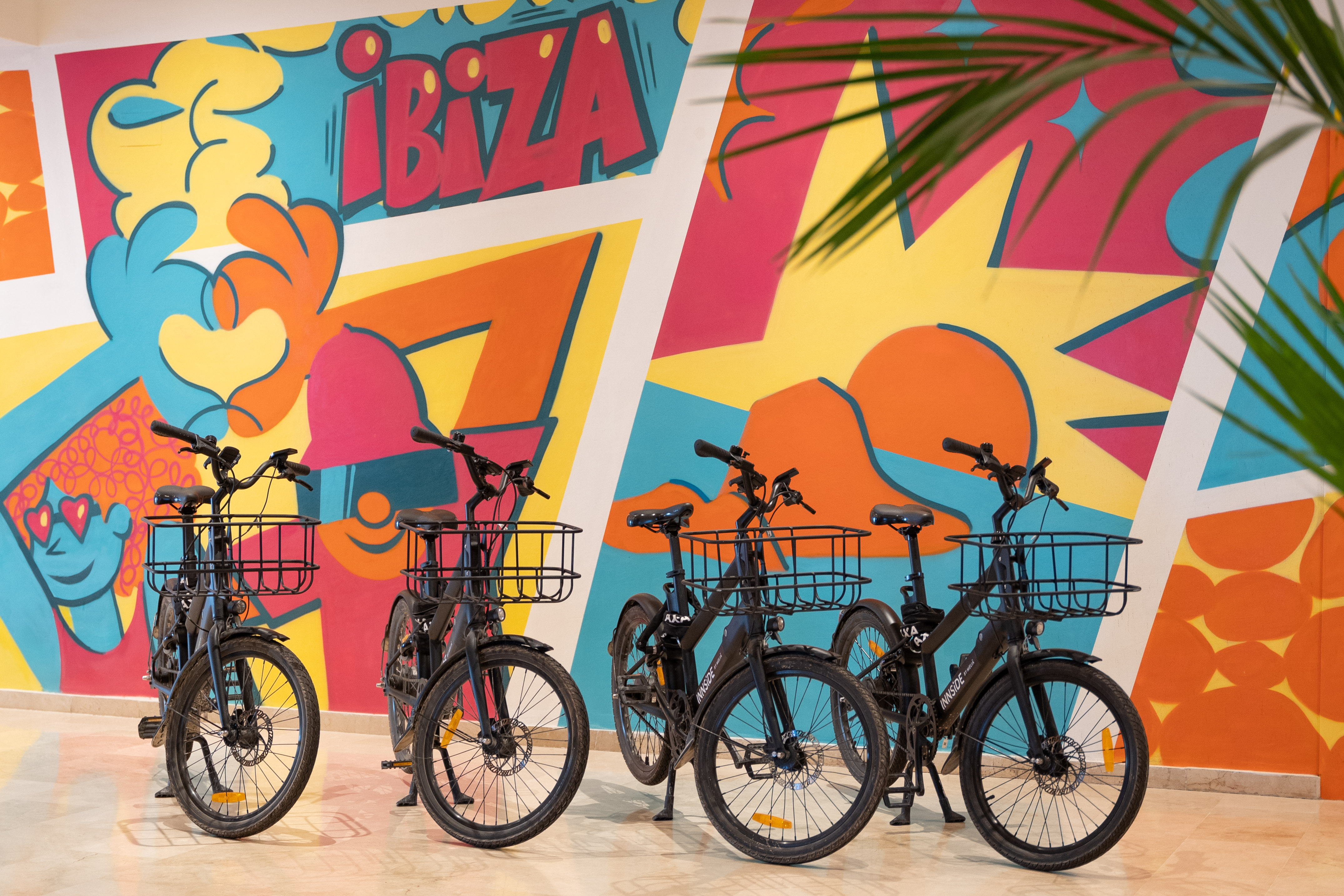Innside black bicycles with baskets against vibrant Ibiza mural.