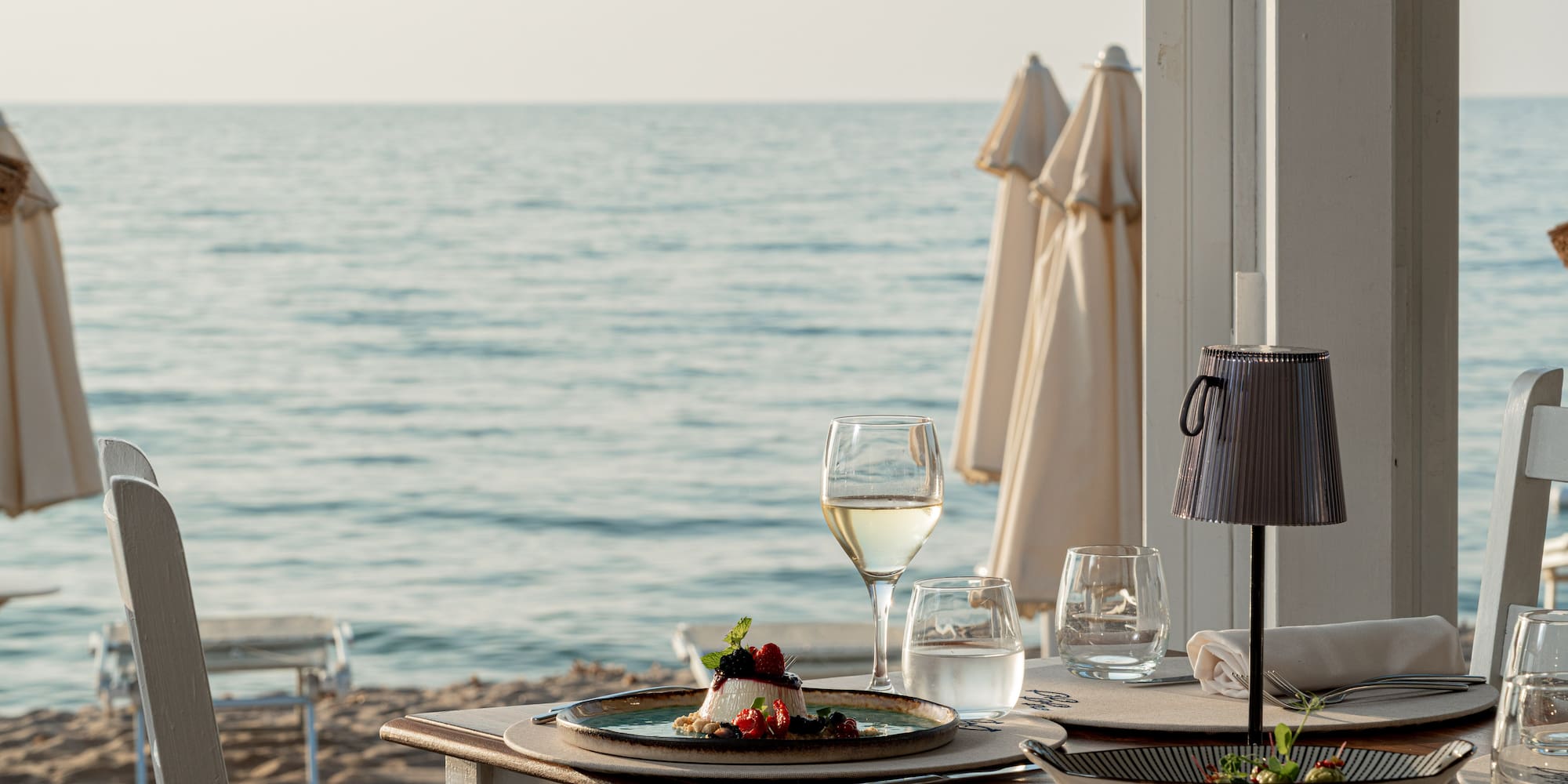 a table with plates of food and glasses of wine on a beach