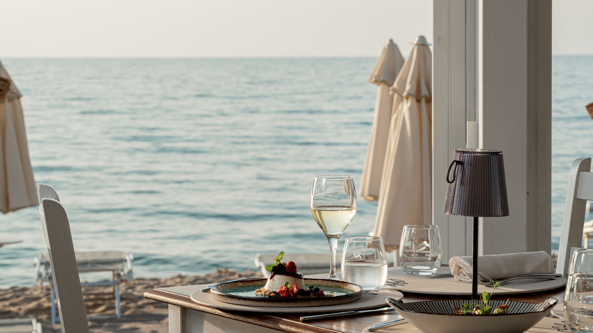 a table with plates of food and glasses of wine on a beach