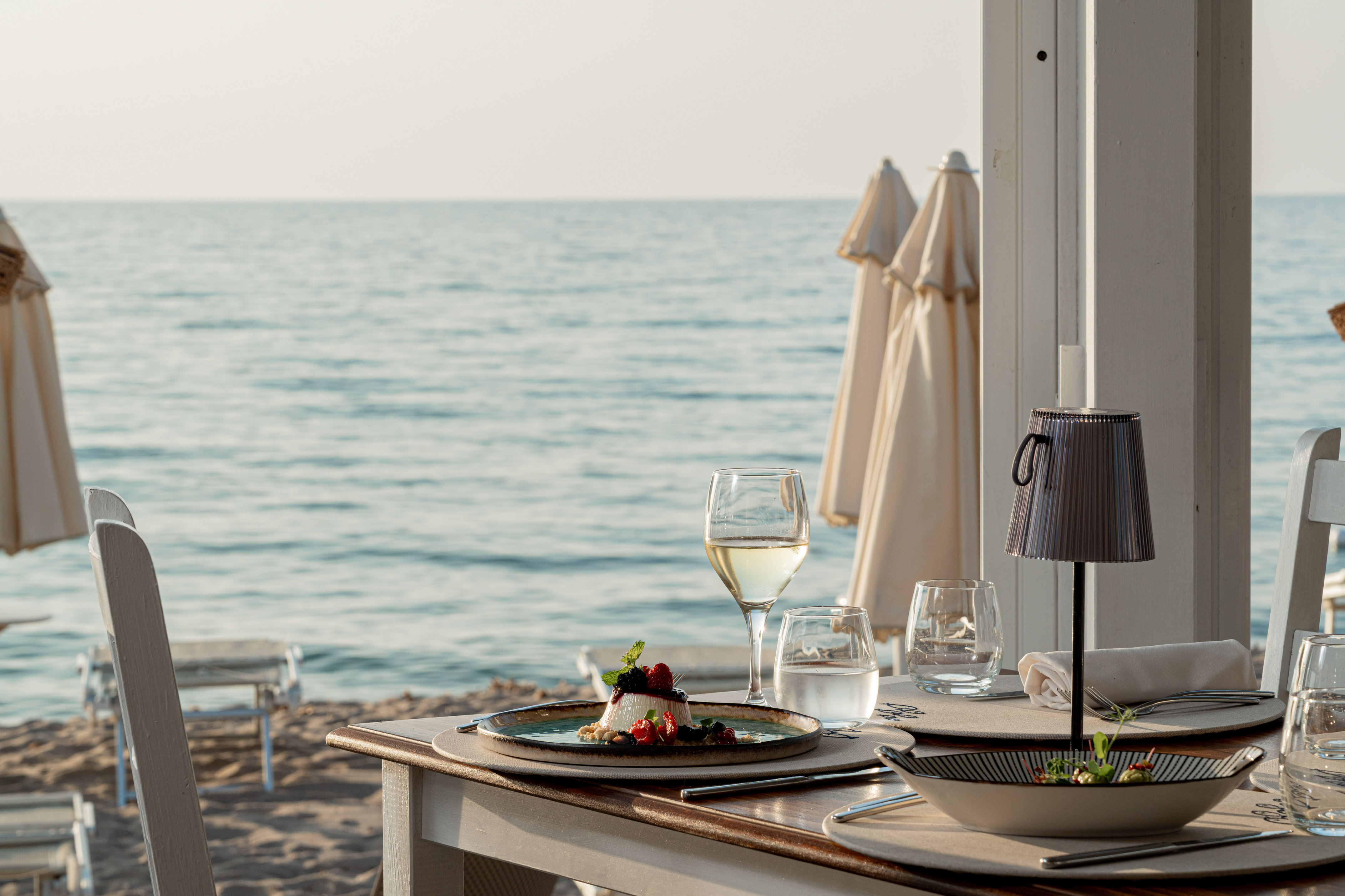 Beachside dining table with dessert, white wine, and ocean view.