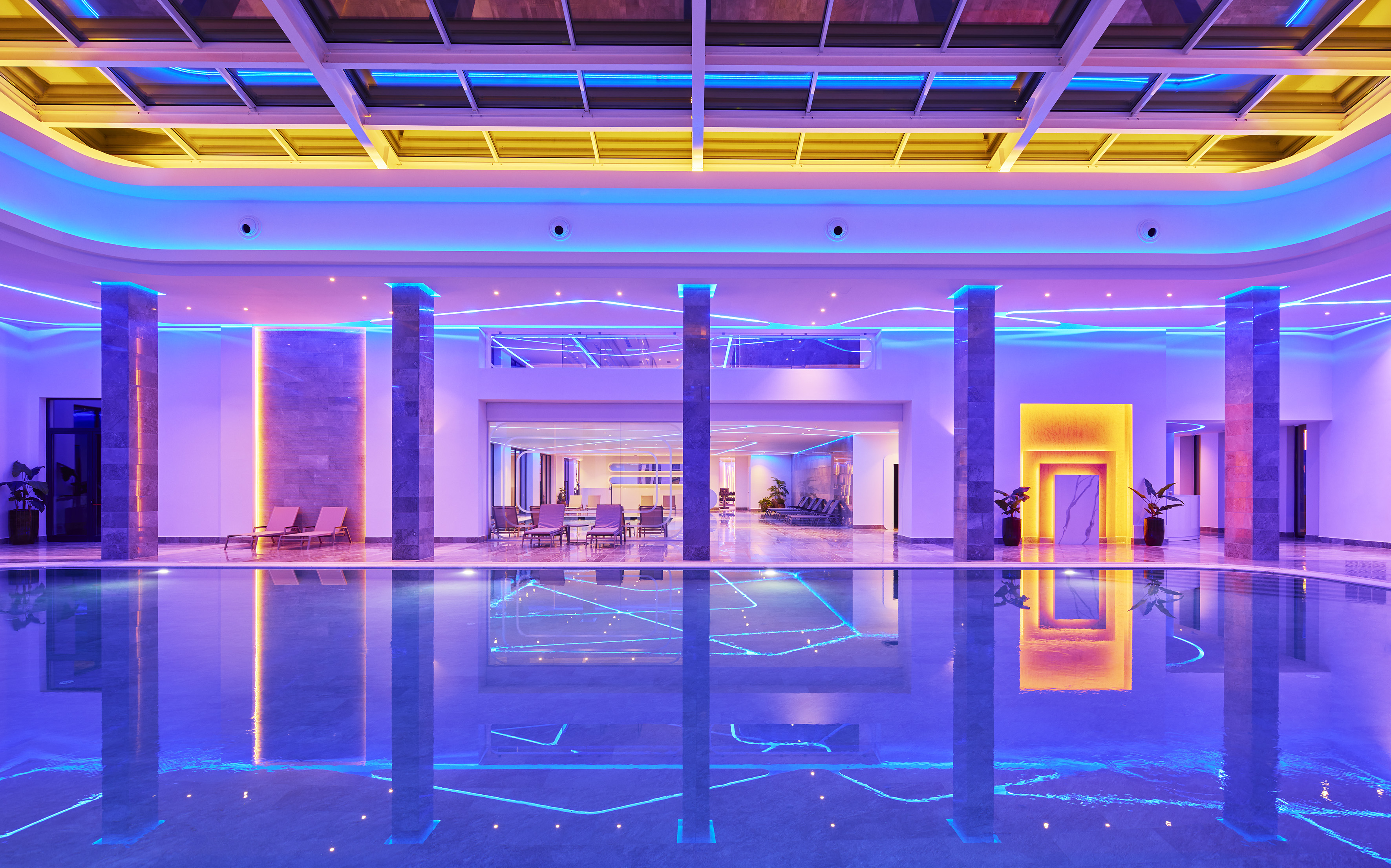 Modern indoor pool with vibrant blue, purple, and yellow LED lighting.