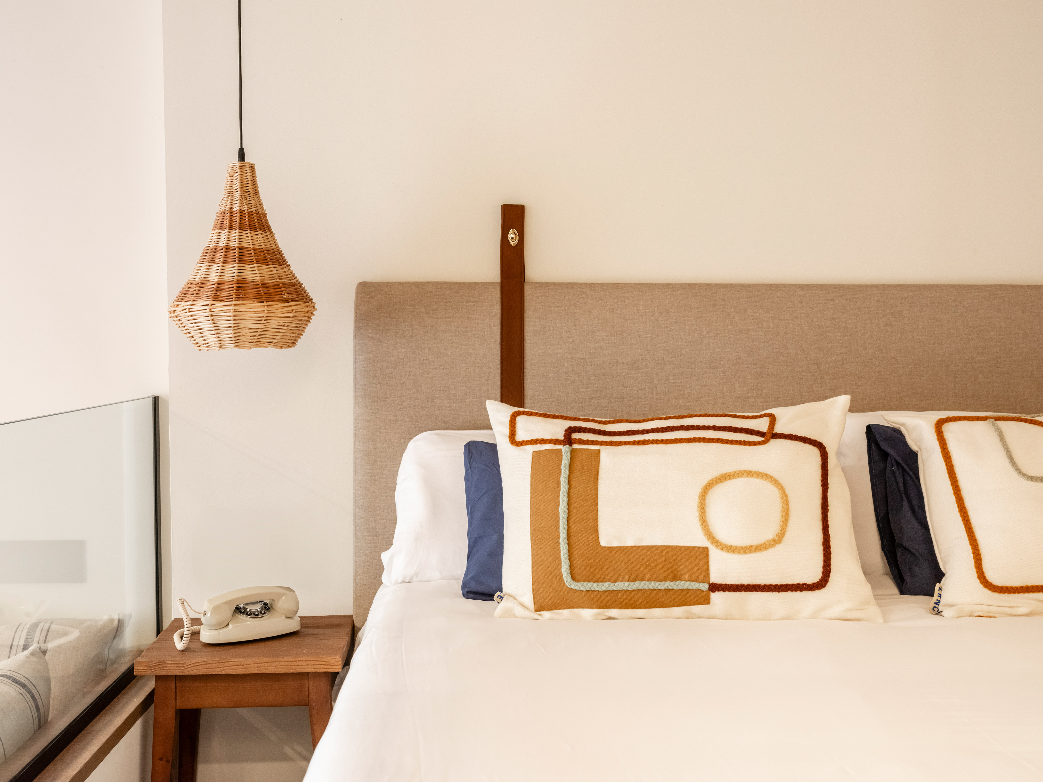 Stylish bedroom with wicker pendant, bed, geometric pillows, and vintage phone.