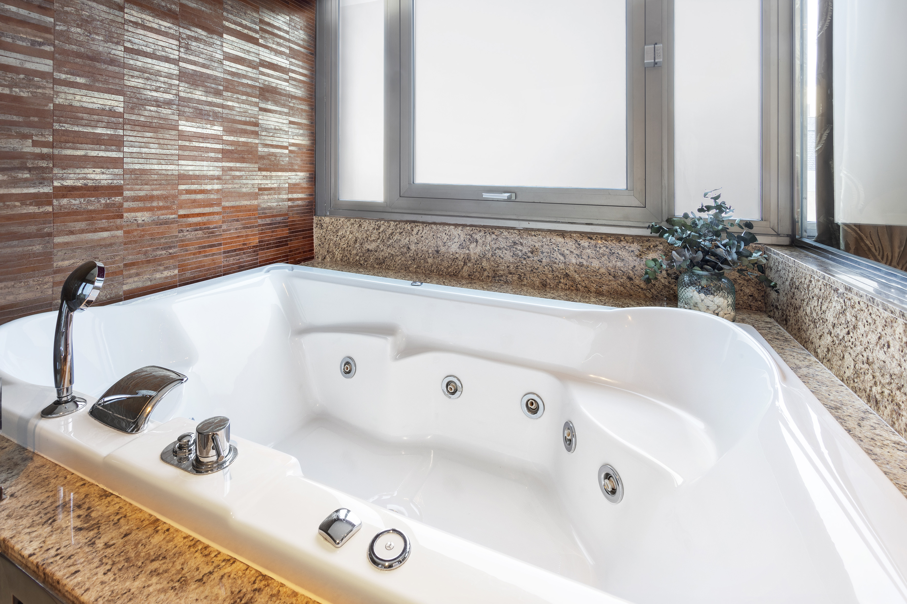 Jacuzzi spa blanco en baño de lujo con azulejos y granito.