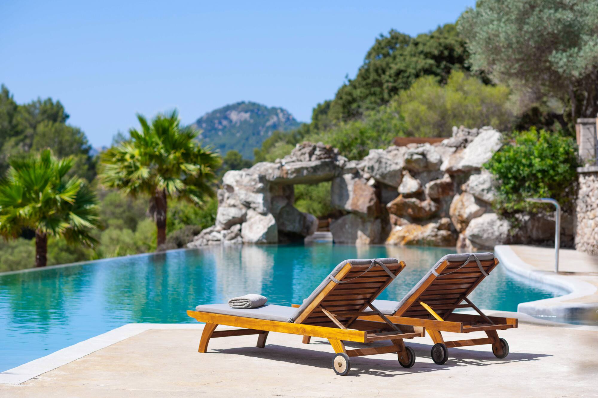 Tropical infinity pool with lounge chairs, palm trees, and rock formations.