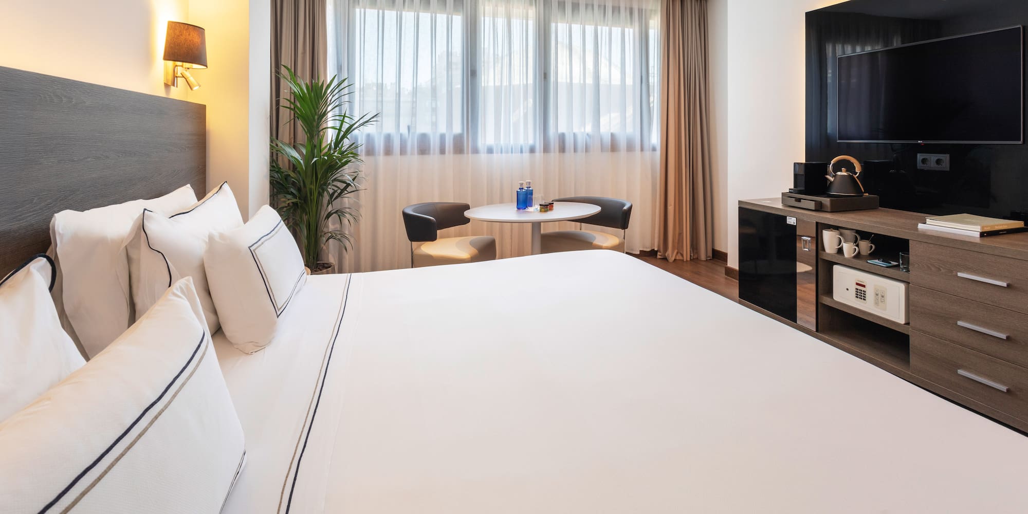 Stylish hotel room with king bed, large window, seating area, and TV cabinet.