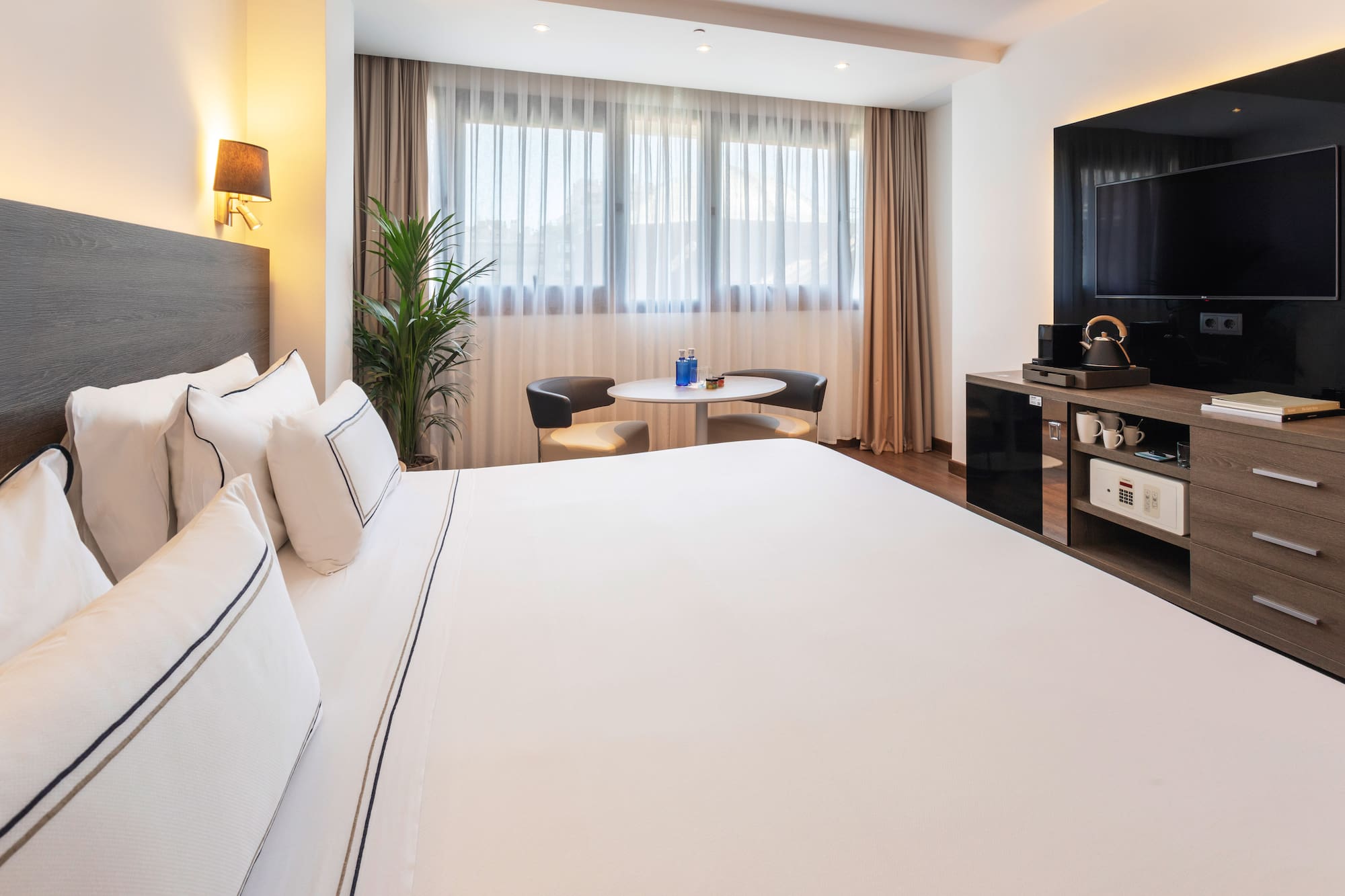 Stylish hotel room with king bed, large window, seating area, and TV cabinet.
