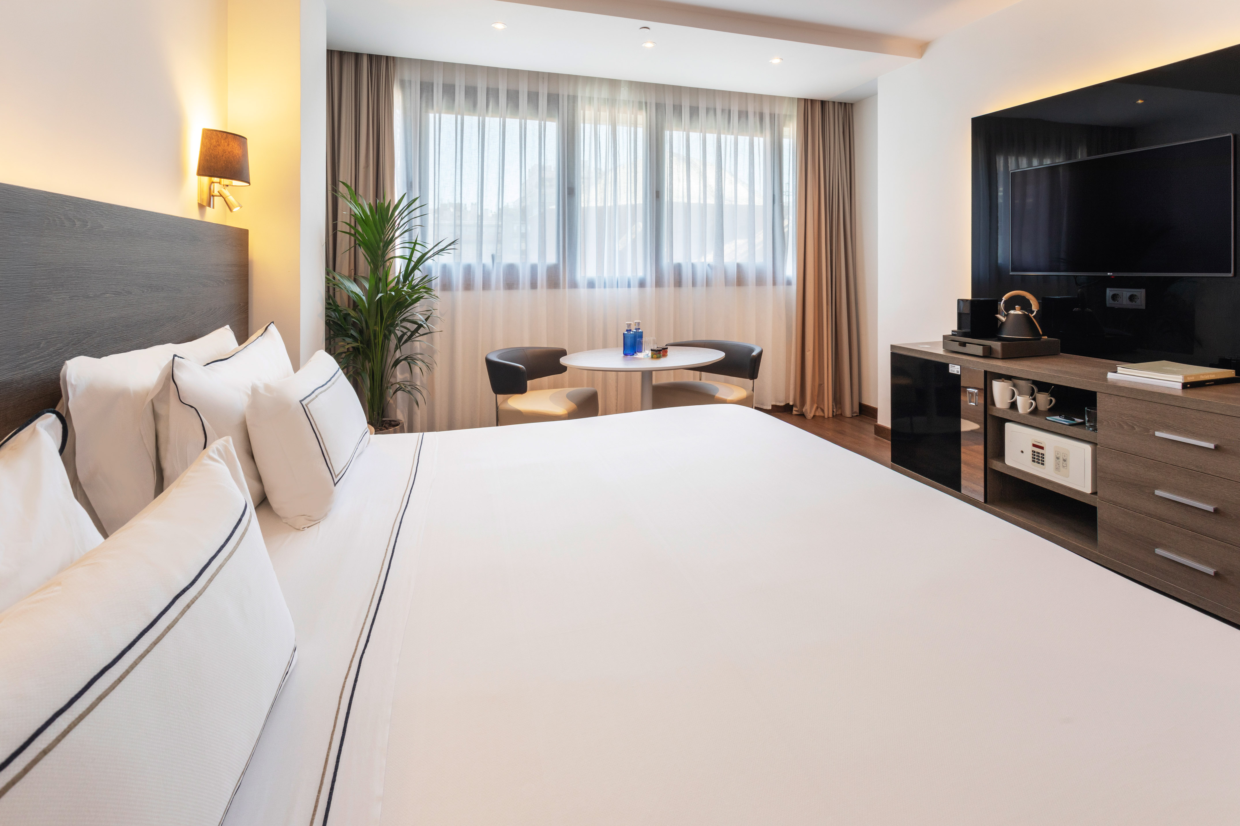 Stylish hotel room with king bed, large window, seating area, and TV cabinet.