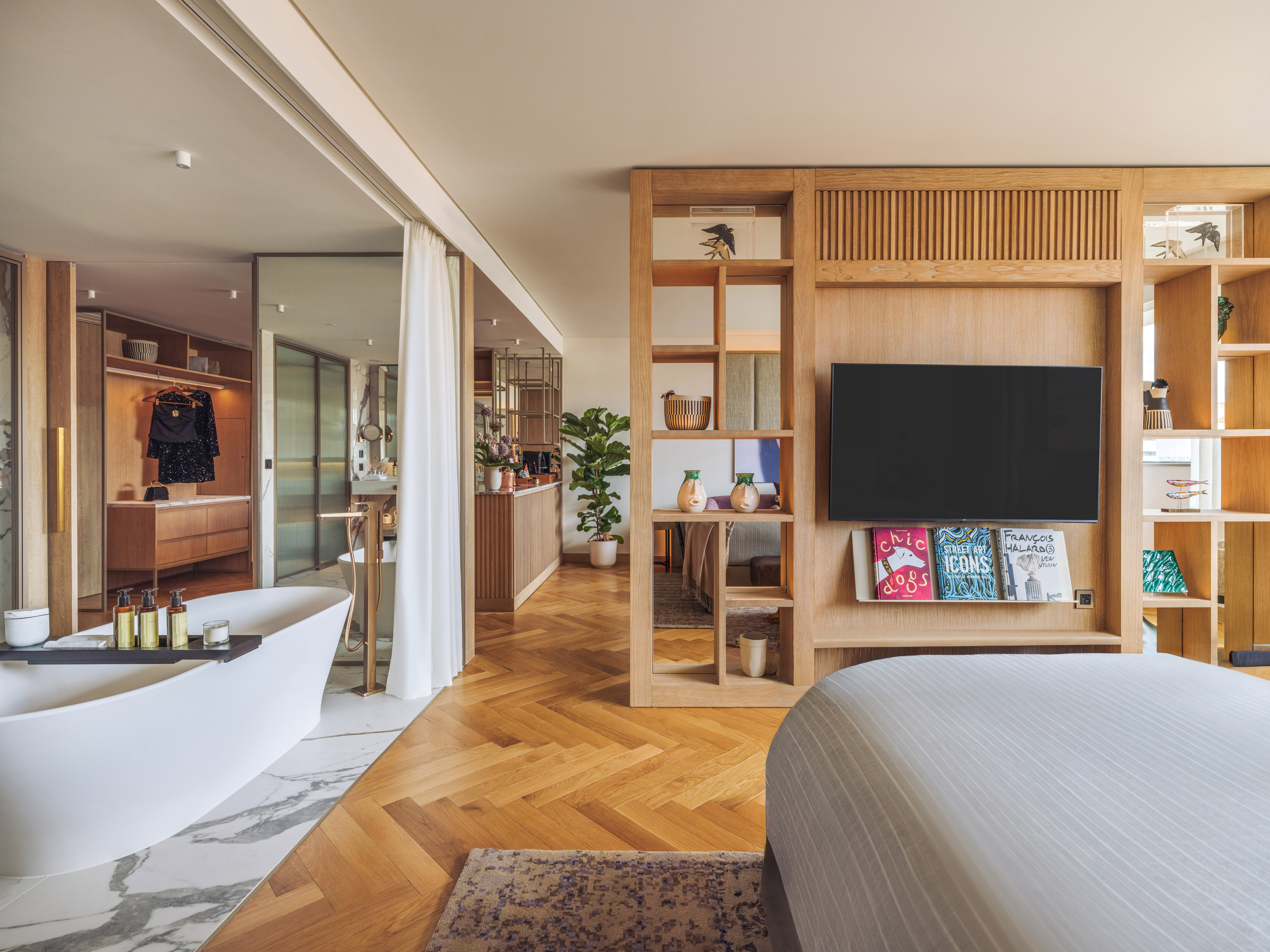 Luxury hotel suite with open-plan bedroom, modern freestanding tub, and wood accents.