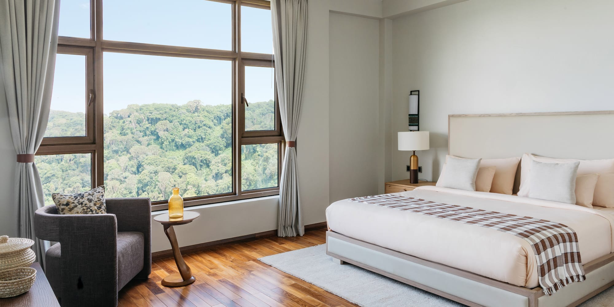 Modern hotel bedroom with forest view, king bed, and hardwood floor.